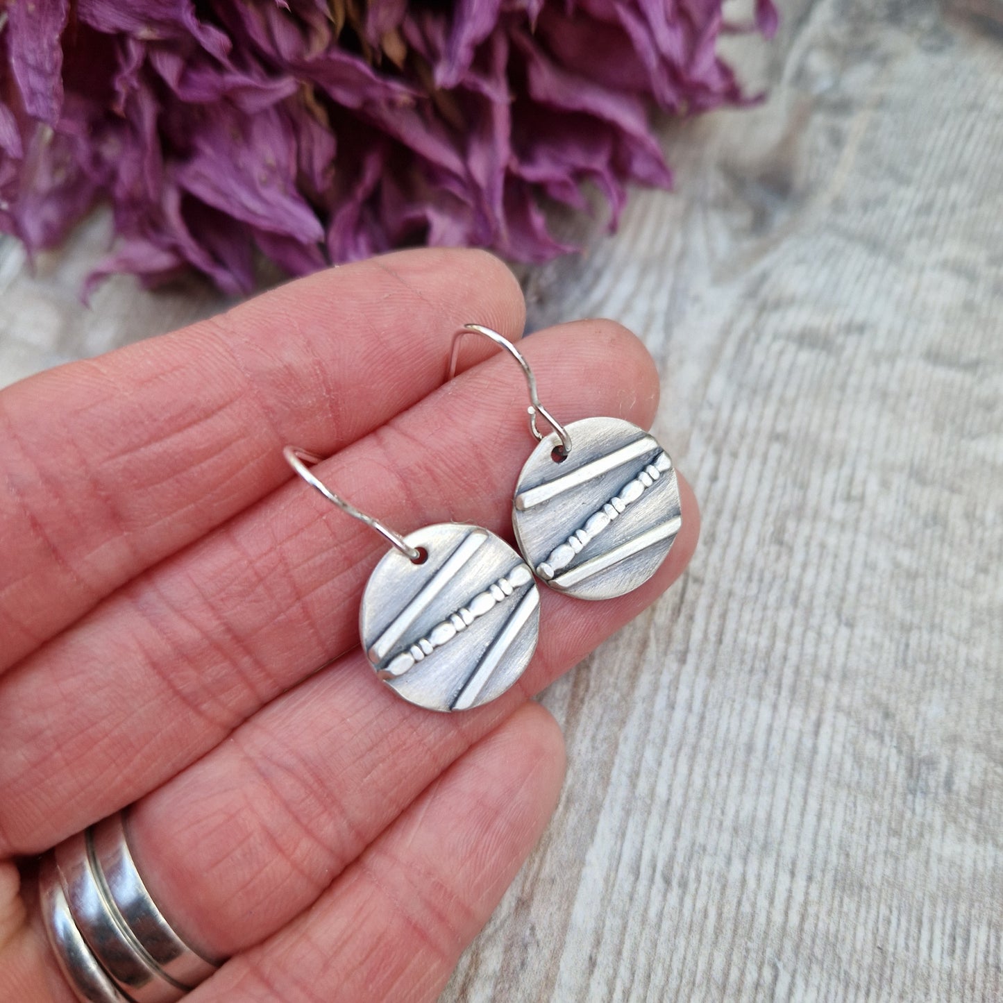 Each earring is an oxidised Sterling Silver disc with one raised straight line, one raised beaded line and one raised straight line at angles to each other across the disc, attached to earring wire.