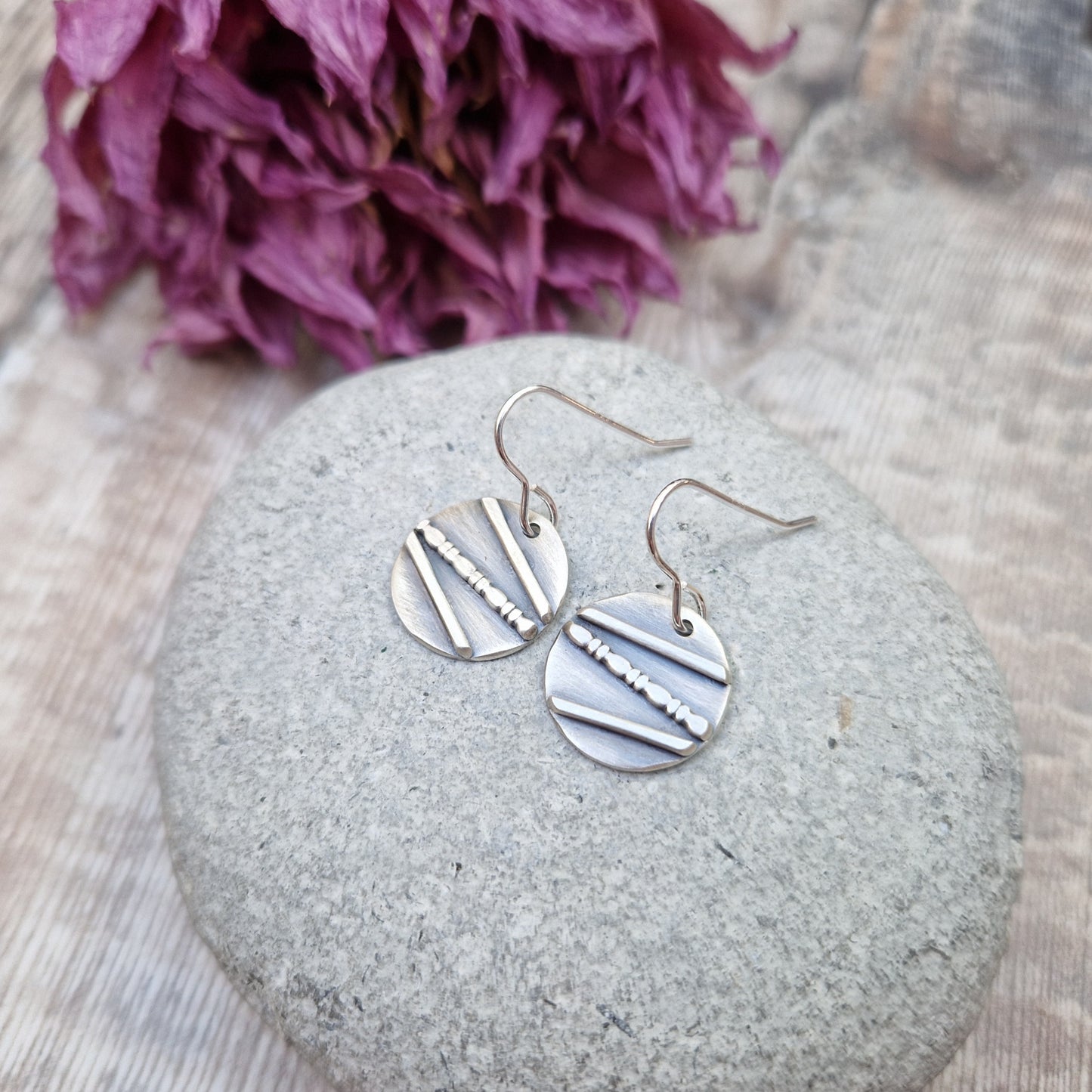 Each earring is an oxidised Sterling Silver disc with one raised straight line, one raised beaded line and one raised straight line at angles to each other across the disc, attached to earring wire.