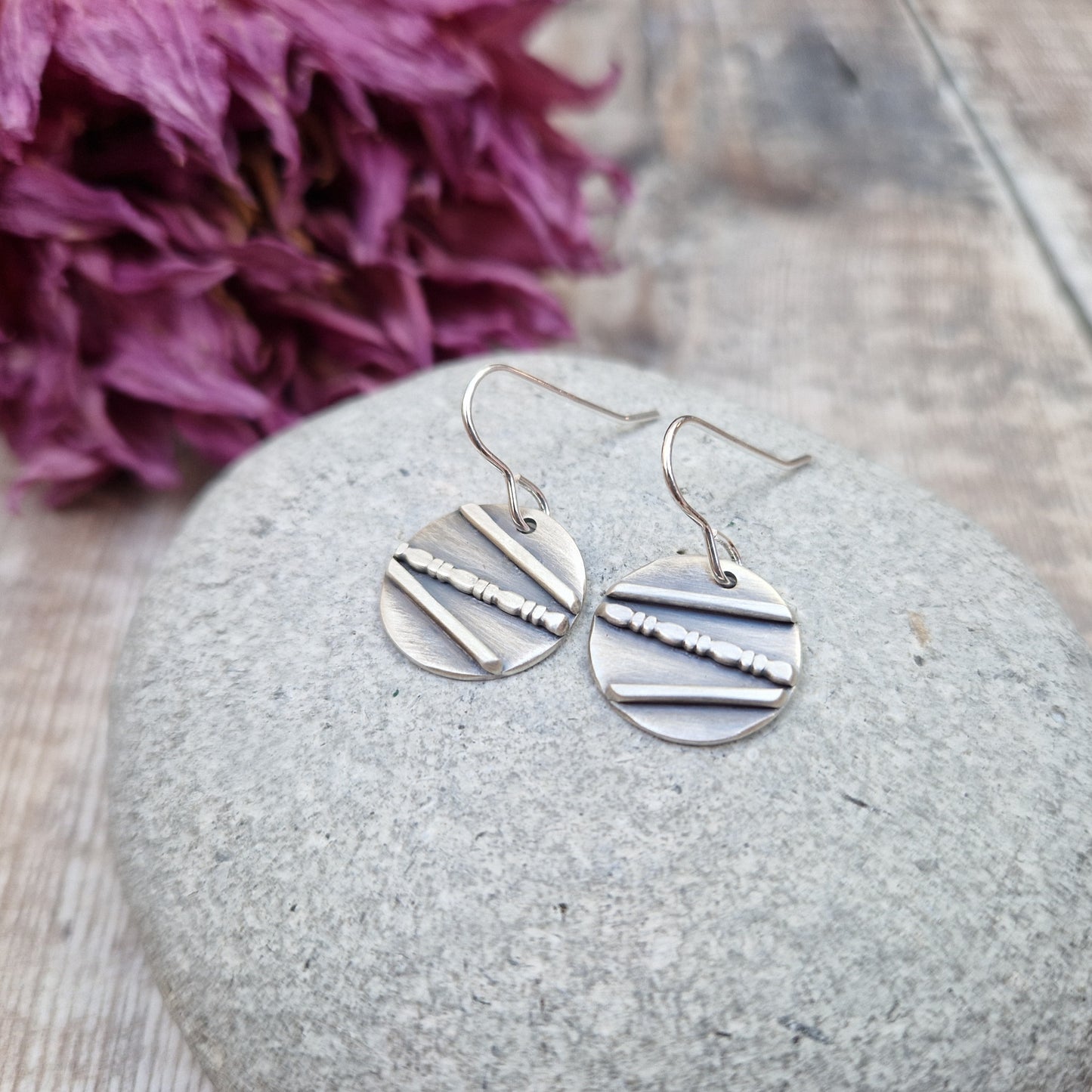 Each earring is an oxidised Sterling Silver disc with one raised straight line, one raised beaded line and one raised straight line at angles to each other across the disc, attached to earring wire.