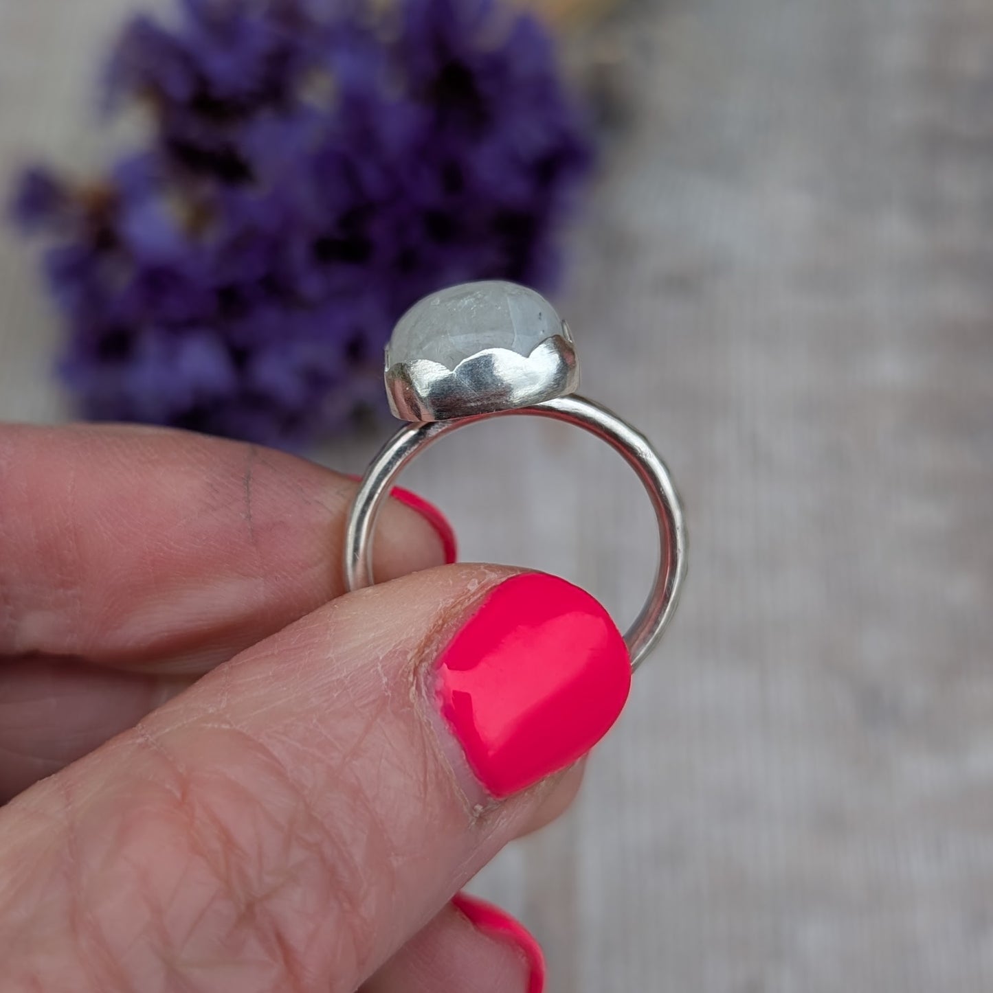 Side view of a Silver Moonstone Ring held between fingers, showing the height of the stone and smooth handmade setting.