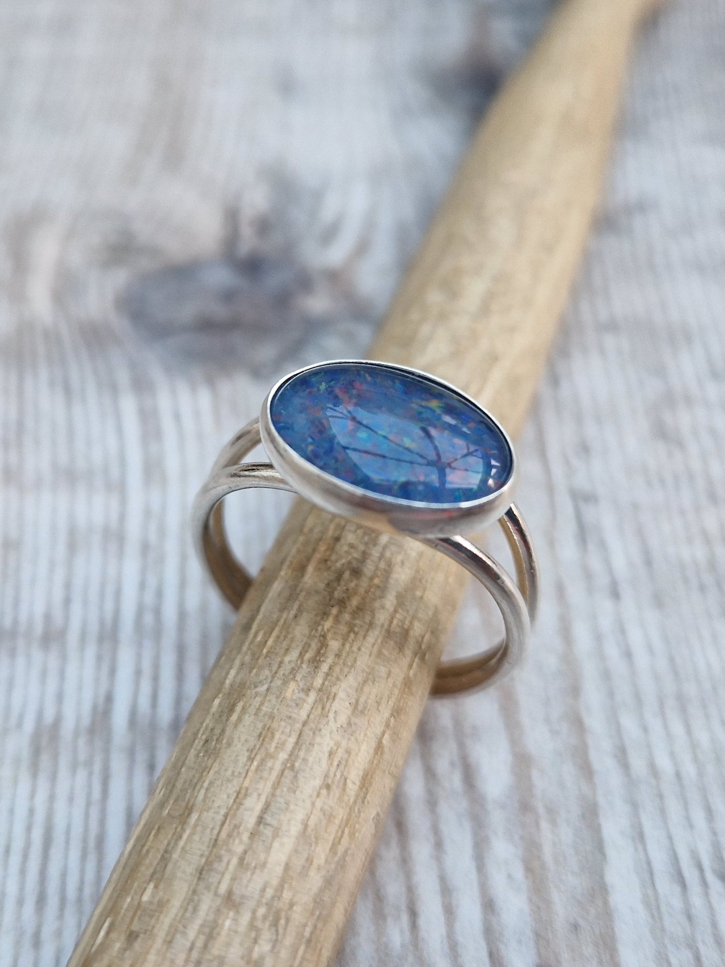 Blue Opal gemstone ring UK Size T ½ oval shape. Midnight blue stone with small flecks of green and orange, set in simple silver bezel surround and mounted lengthways on two silver bands that split at front and come together at back.