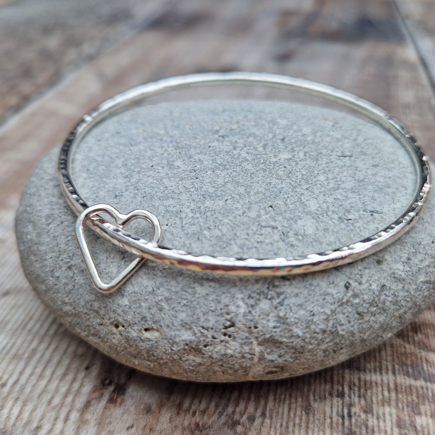 Sterling Silver bangle with hammered texture finish. Bangle passes through an open open-heart shape.