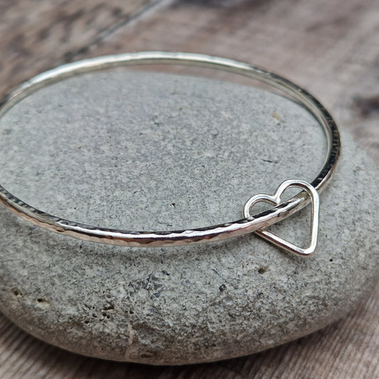 Sterling Silver bangle with hammered texture finish. Bangle passes through an open open-heart shape.