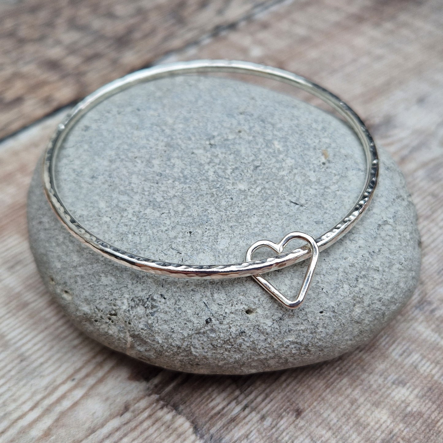 Sterling Silver bangle with hammered texture finish. Bangle passes through an open open-heart shape.