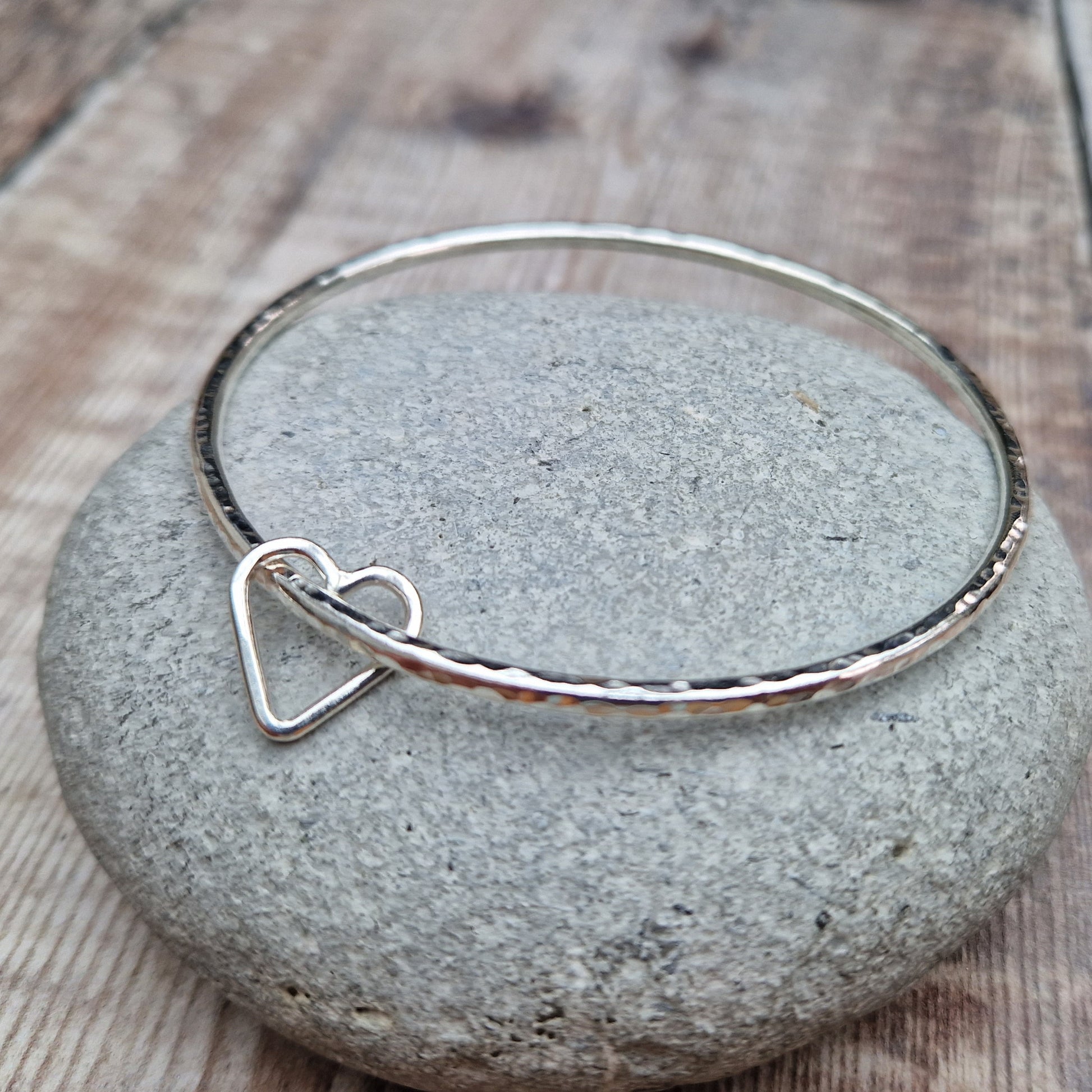 Sterling Silver bangle with hammered texture finish. Bangle passes through an open open-heart shape.