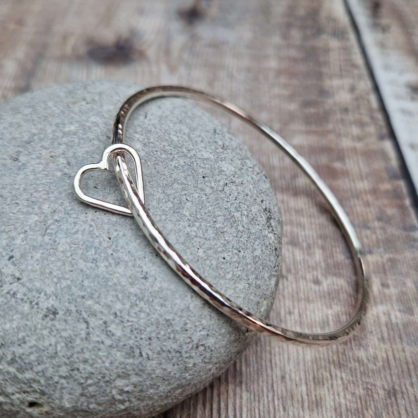 Sterling Silver bangle with hammered texture finish. Bangle passes through an open open-heart shape.