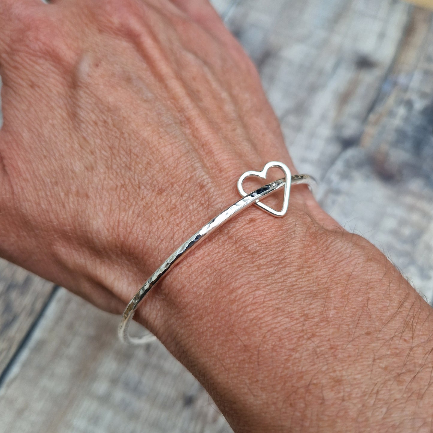 Sterling Silver bangle with hammered texture finish. Bangle passes through an open open-heart shape.