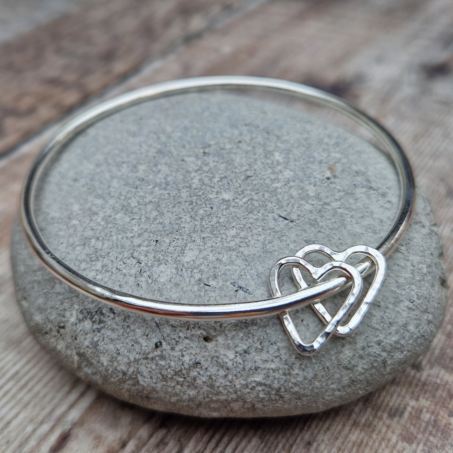 Sterling Silver bangle with two silver open heart shapes with hammered finish. Bangle passes through the open-heart shapes.