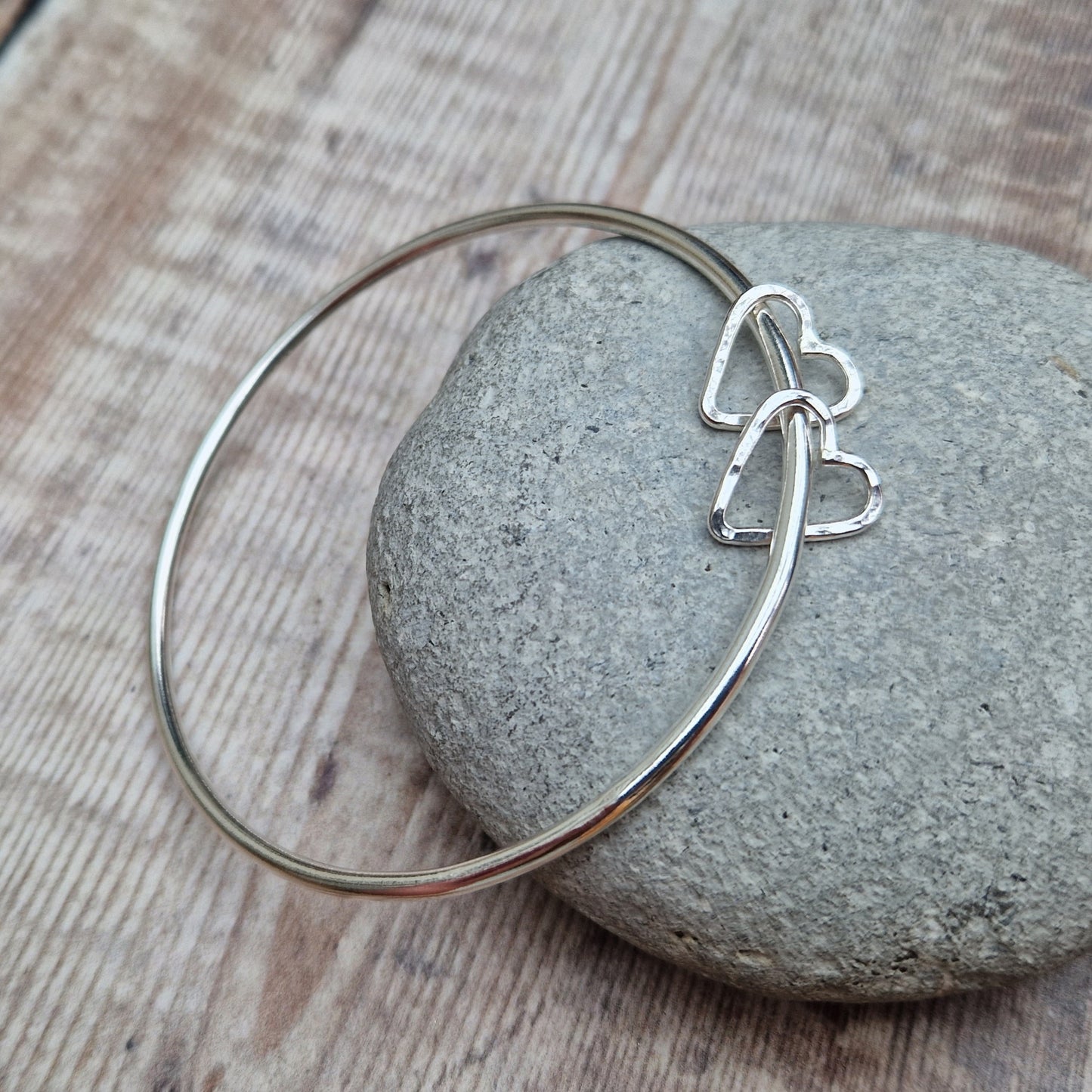 Sterling Silver bangle with two silver open heart shapes with hammered finish. Bangle passes through the open-heart shapes.