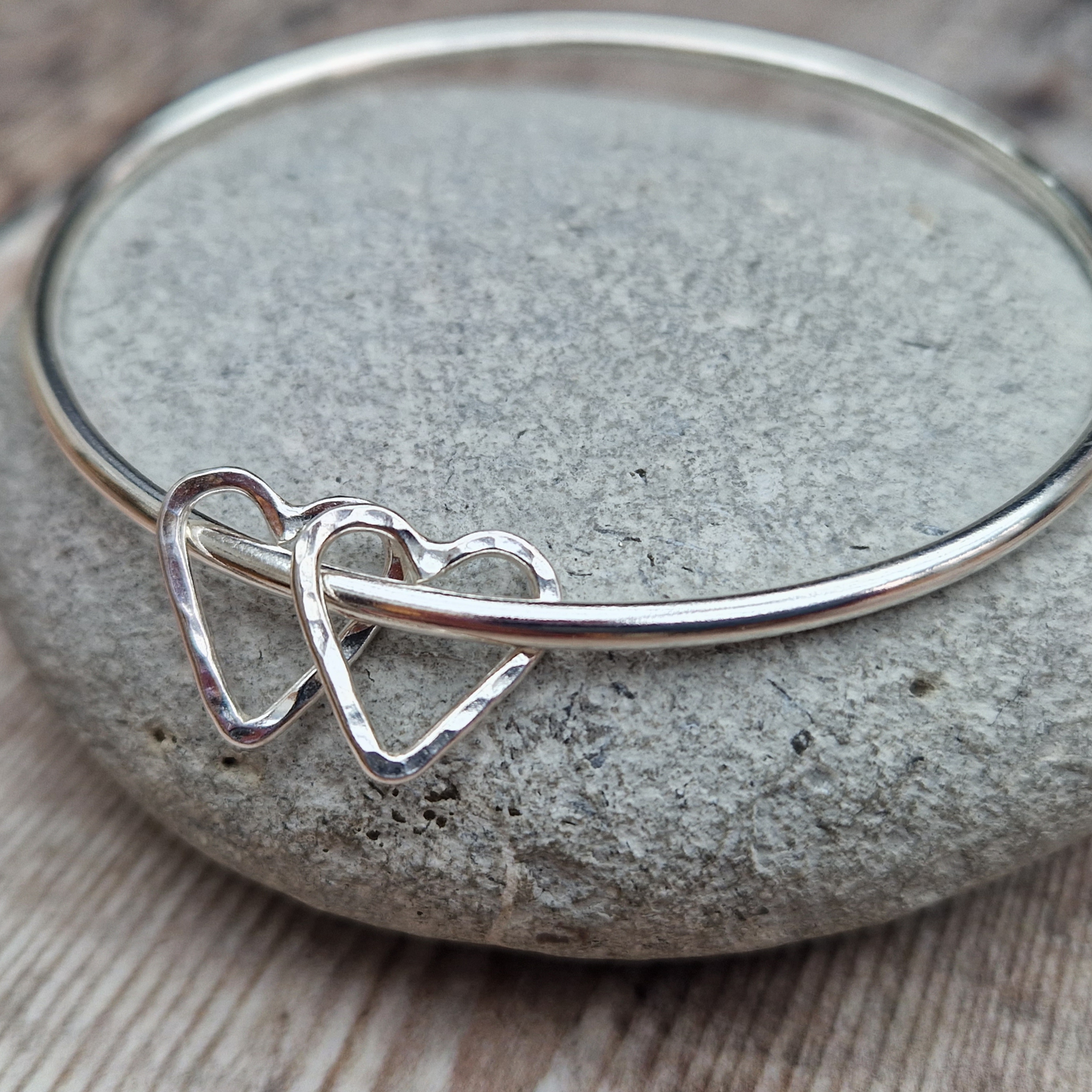 Sterling Silver bangle with two silver open heart shapes with hammered finish. Bangle passes through the open-heart shapes.