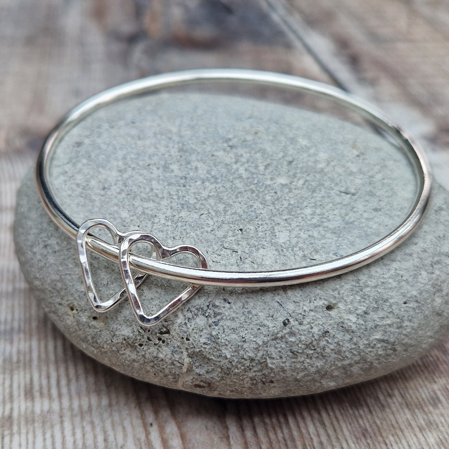 Sterling Silver bangle with two silver open heart shapes with hammered finish. Bangle passes through the open-heart shapes.