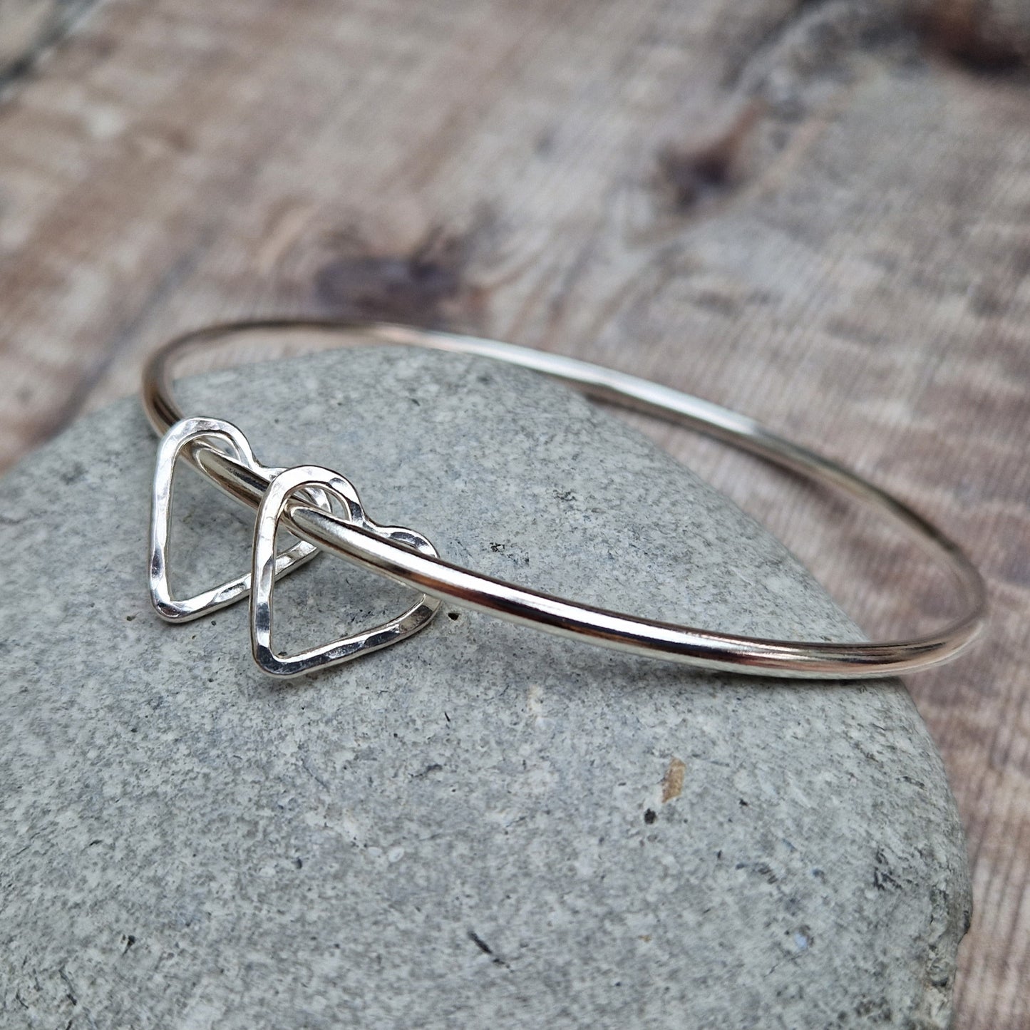 Sterling Silver bangle with two silver open heart shapes with hammered finish. Bangle passes through the open-heart shapes.