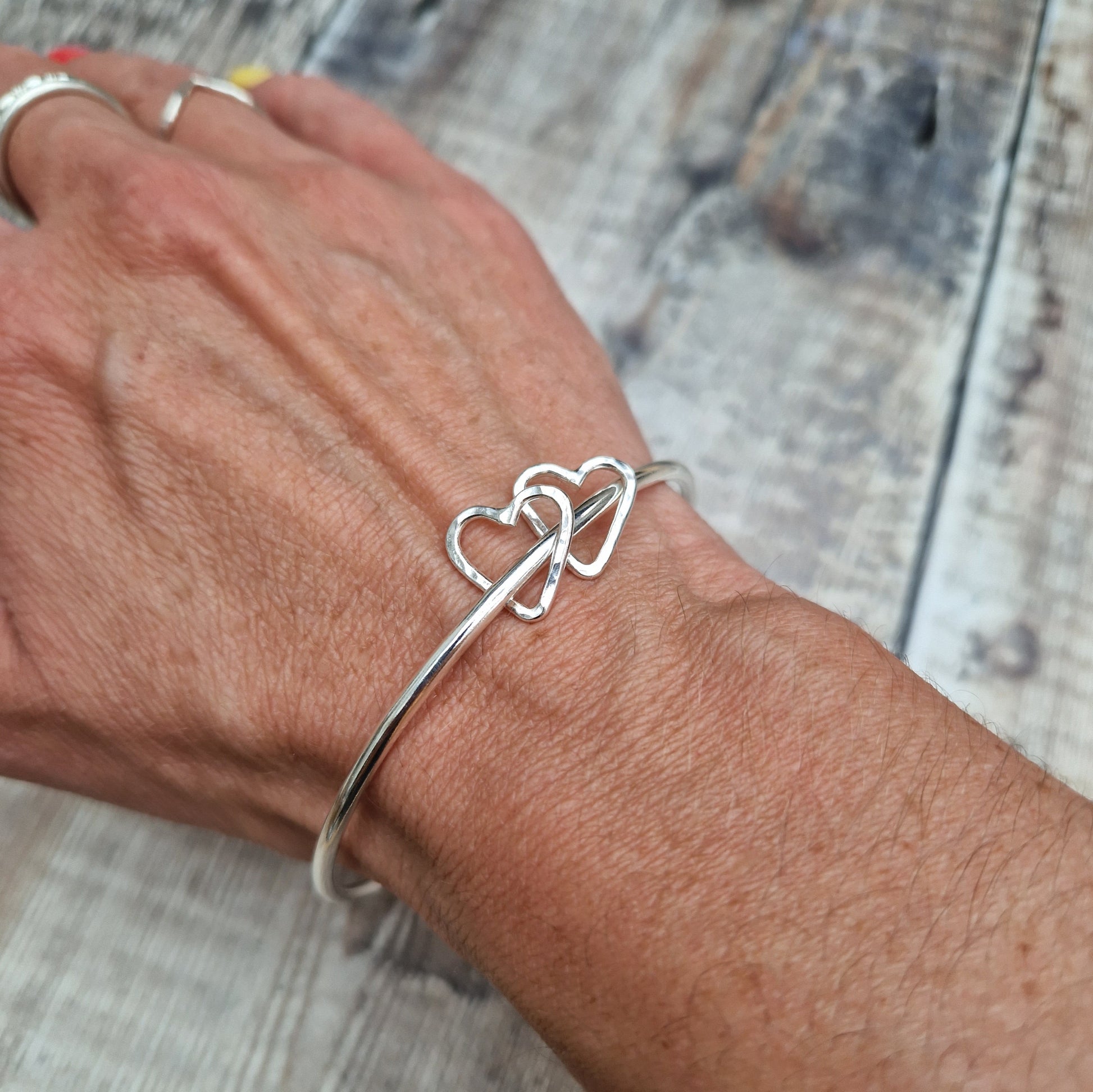 Sterling Silver bangle with two silver open heart shapes with hammered finish. Bangle passes through the open-heart shapes.