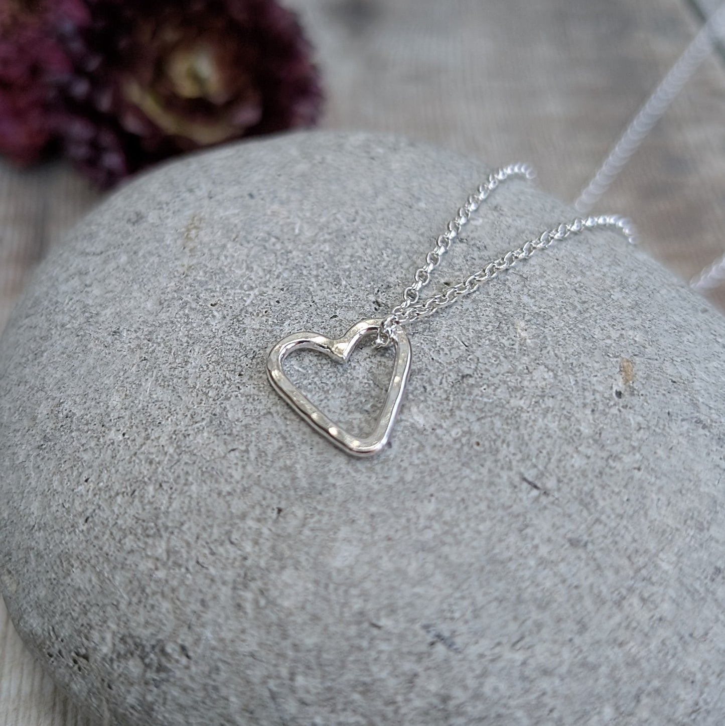 A single hammered silver heart pendant resting on a smooth stone, attached to a fine silver chain.