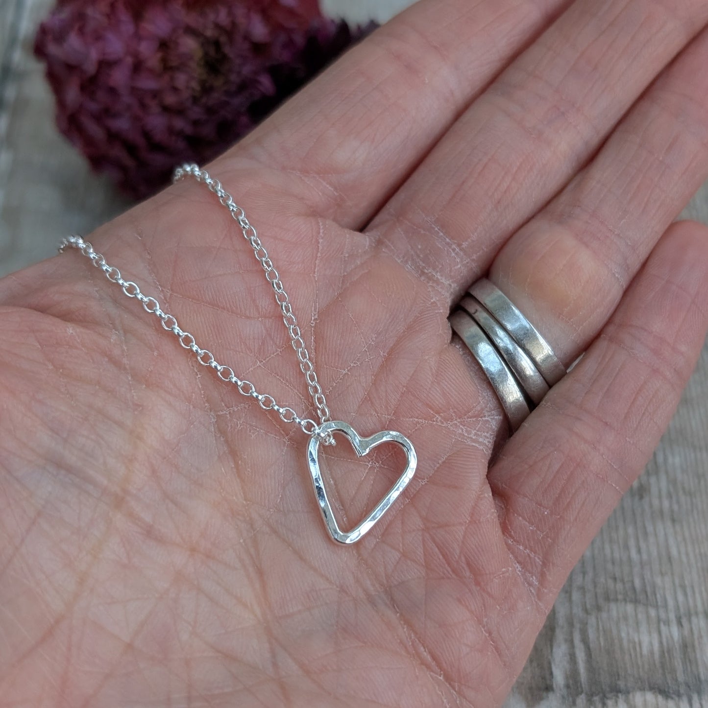 A handmade open heart necklace in recycled sterling silver, displayed on a hand with a fine silver chain.