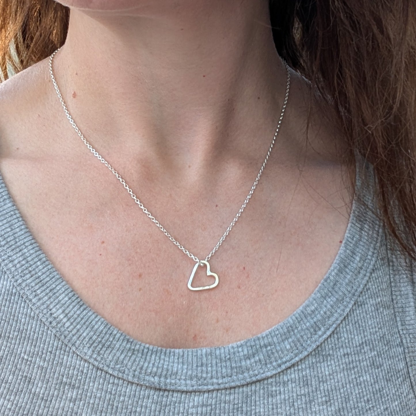 A sterling silver open heart necklace worn on a woman’s neck, showing its delicate and minimalist design.