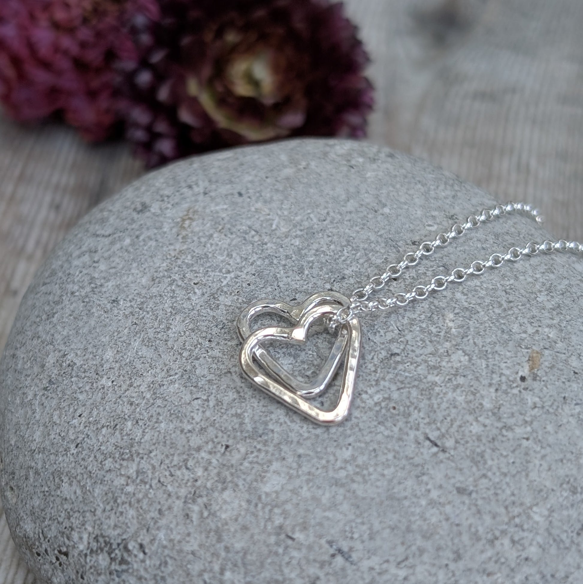 A handmade double heart necklace in sterling silver, featuring two interlinked hammered hearts on a silver chain.