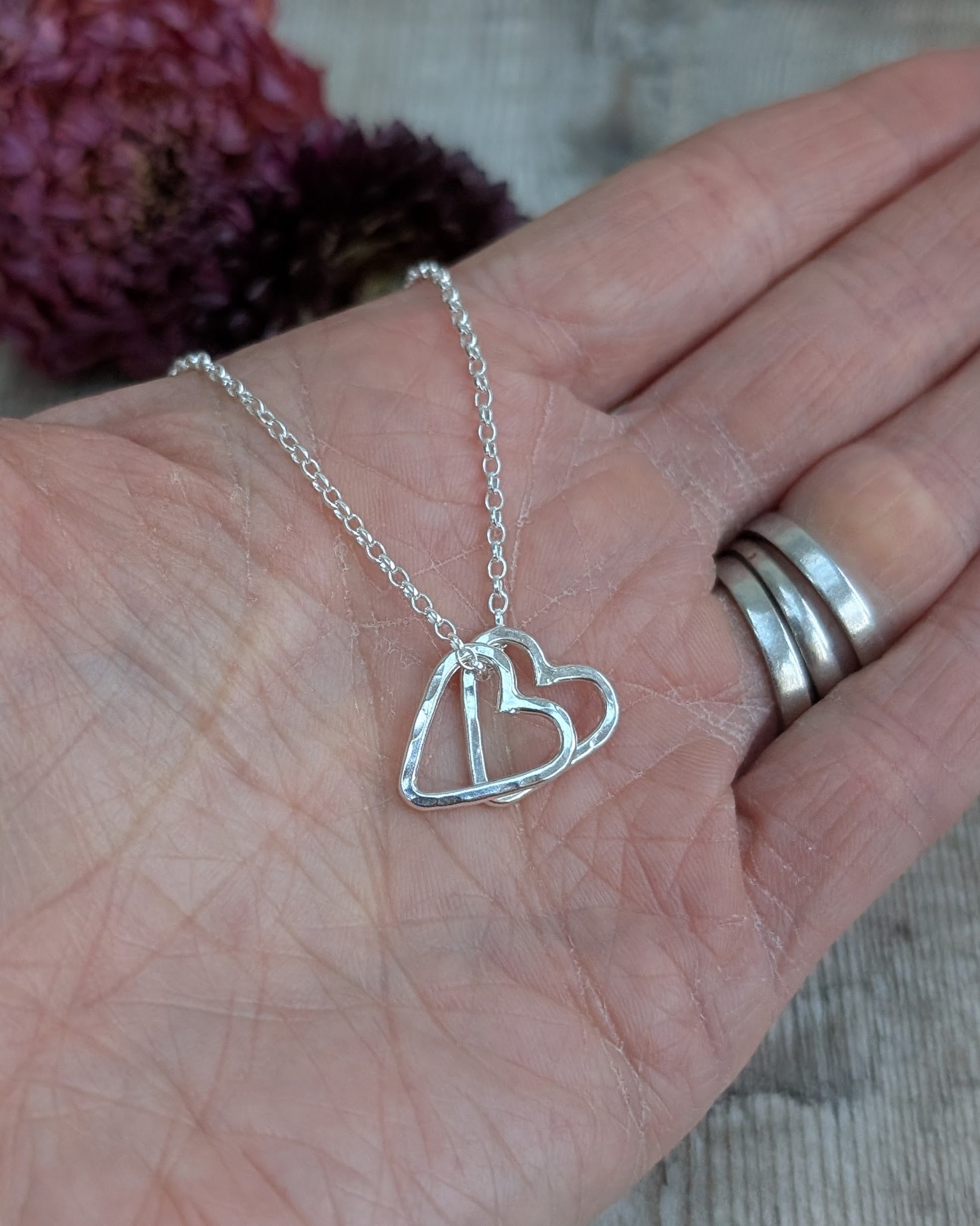 A handmade double heart necklace in sterling silver, featuring two interlinked hammered hearts on a silver chain.