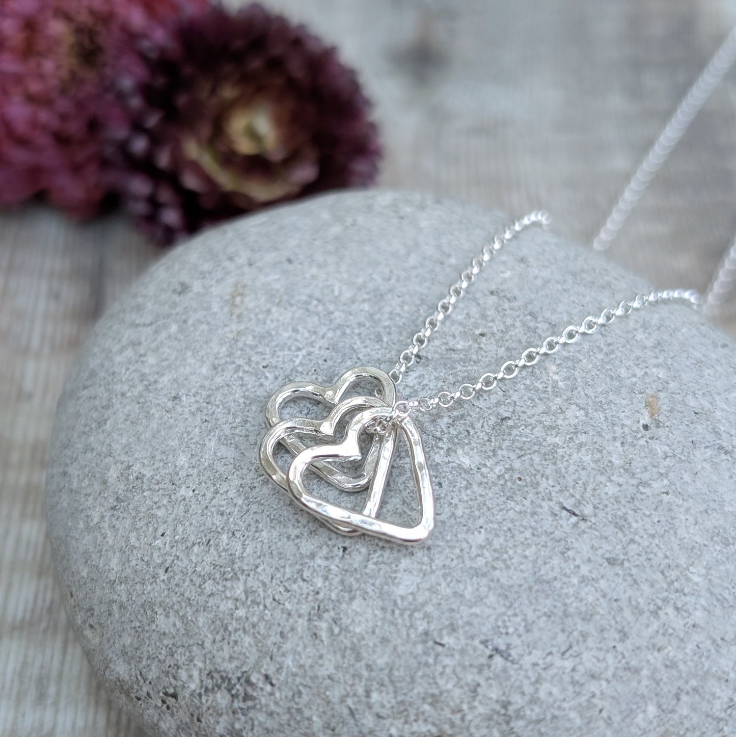 A three-heart hammered silver necklace on a smooth stone, crafted from recycled sterling silver.