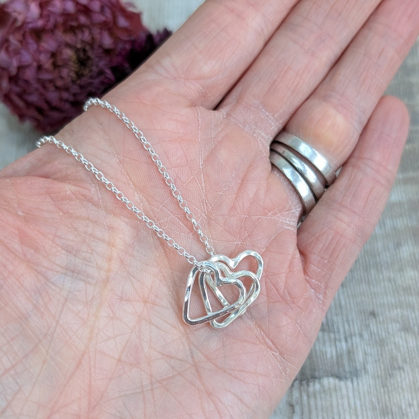 A recycled silver necklace with multiple hammered open hearts, shown resting on a hand.