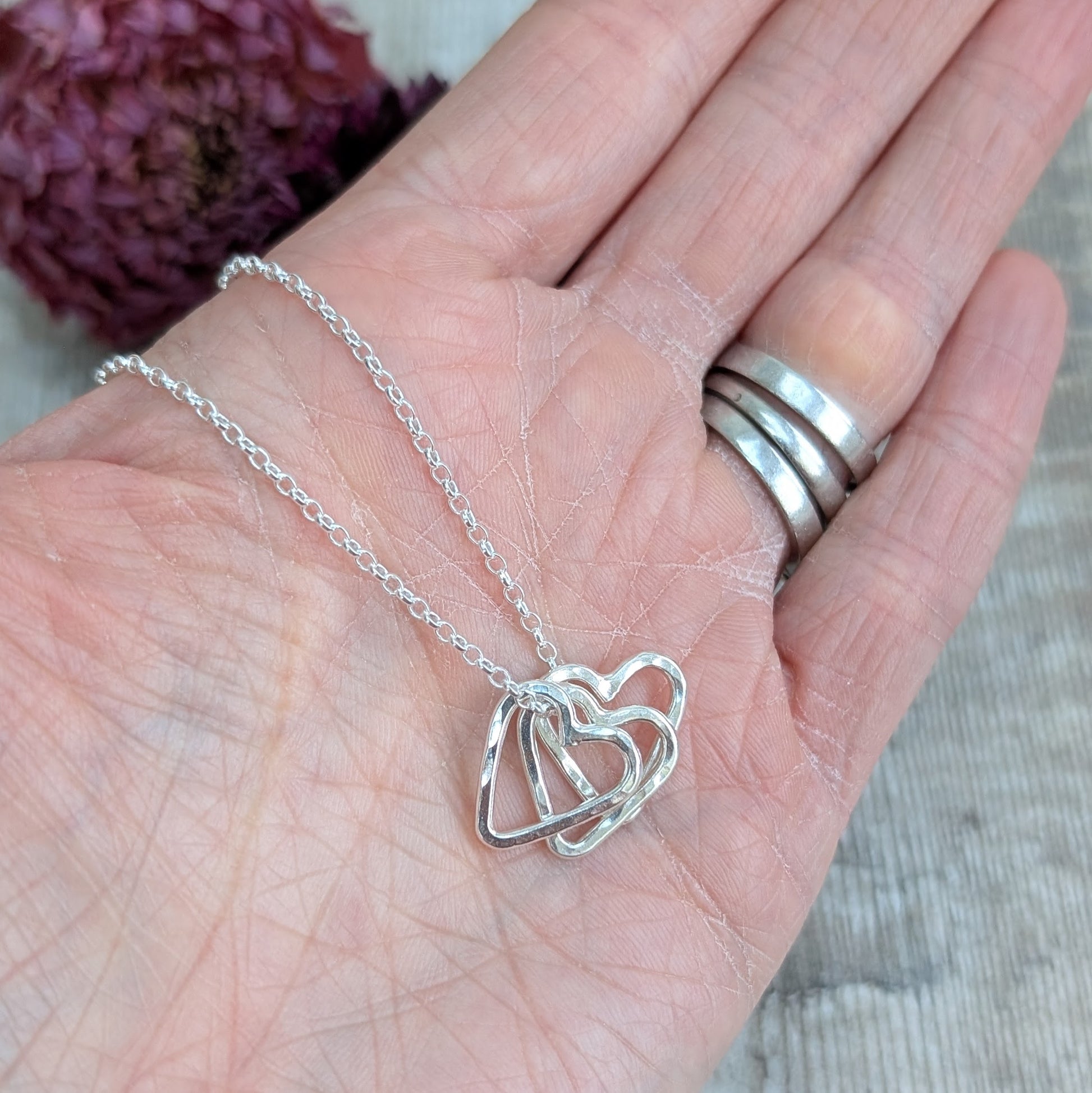 A recycled silver necklace with multiple hammered open hearts, shown resting on a hand.