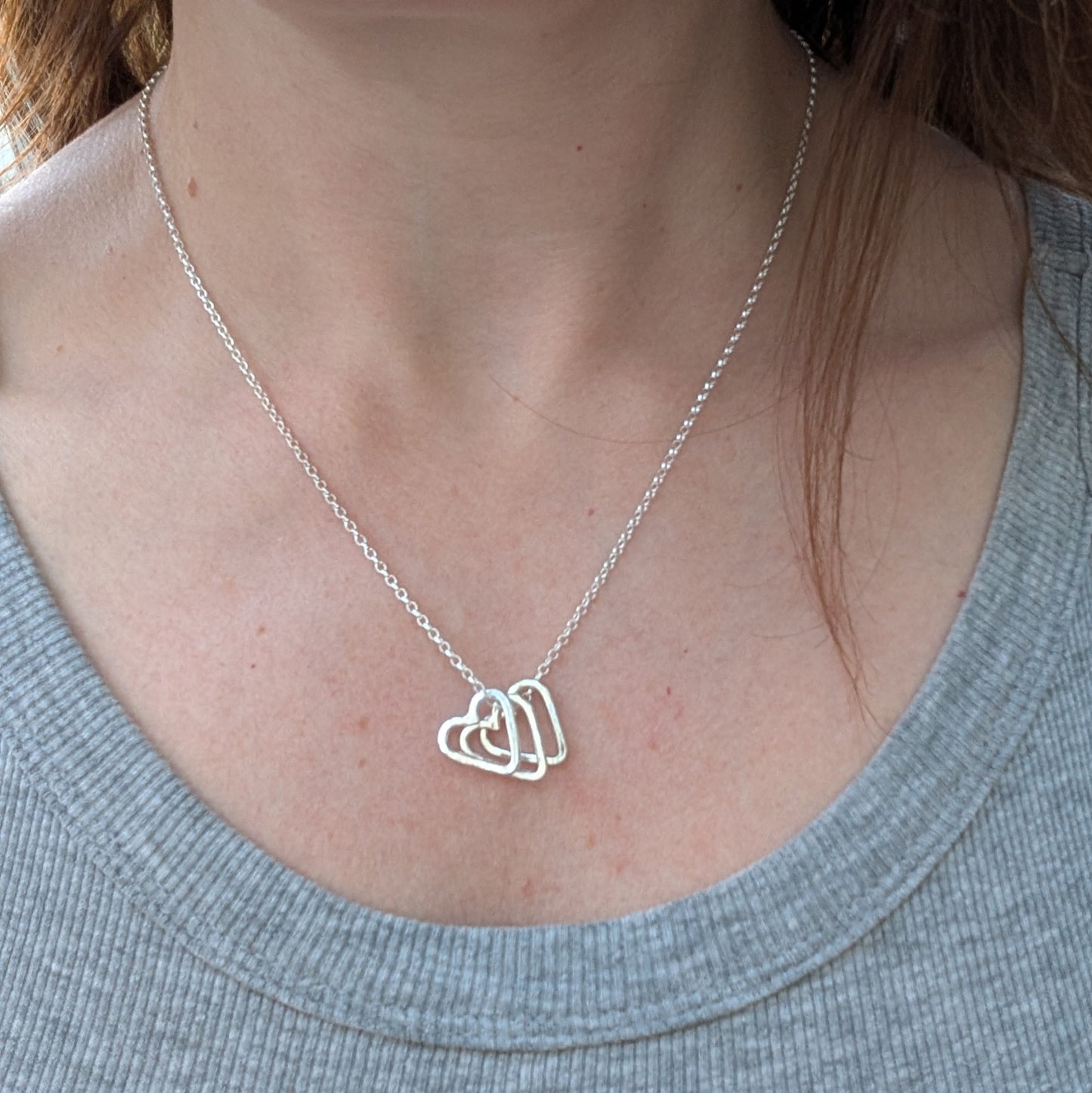 A sterling silver necklace with three open hammered hearts, layered on a silver chain, displayed on a woman’s neck.