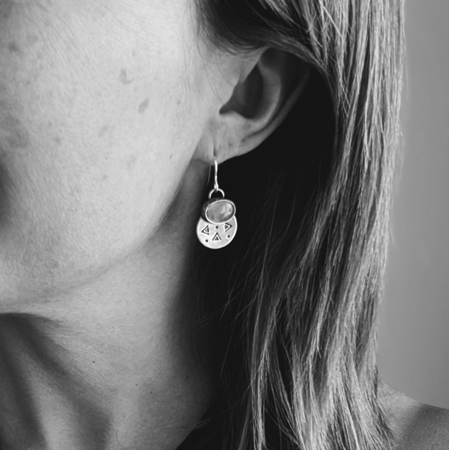 Each earring features one oval-shaped orange opal gemstone with vibrant hues set into an oxidised silver bezel mounted onto a round silver disc with geometric patterns, including small triangles and dots suspended from silver earring wire.