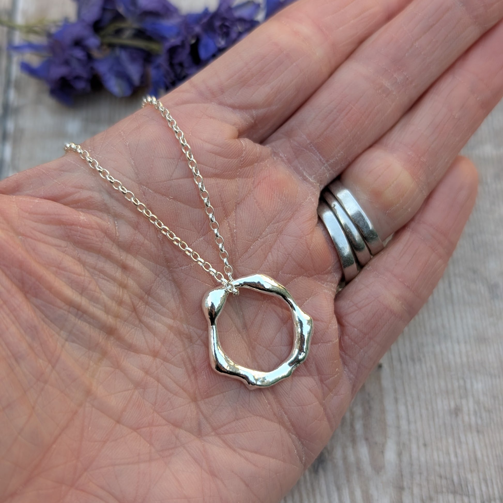 A delicate silver organic open circle pendant necklace displayed in the palm of a hand, showing its size and fine chain detail.