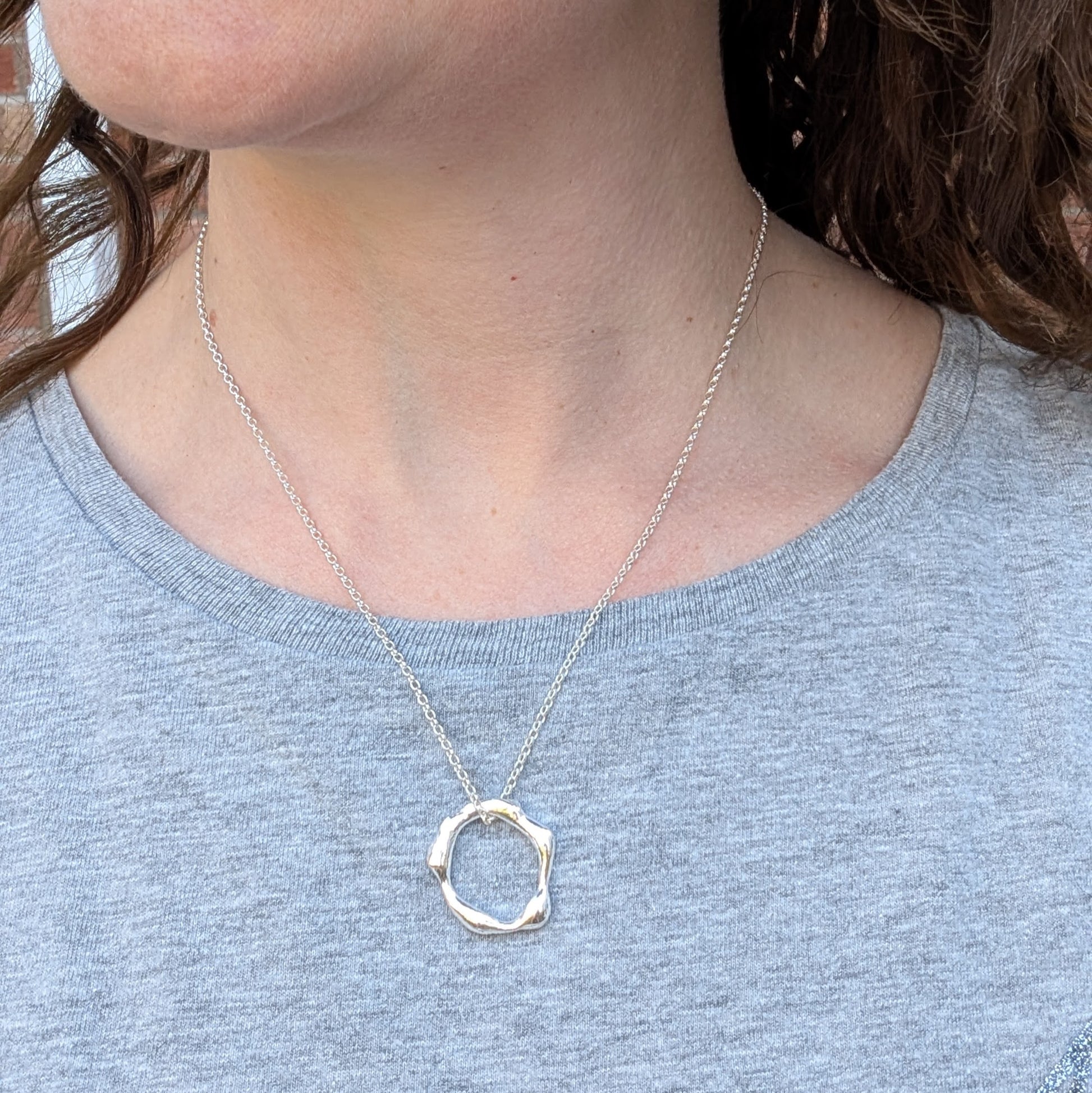A model wearing the organic silver circle necklace on a sterling silver chain, styled with a casual grey top.