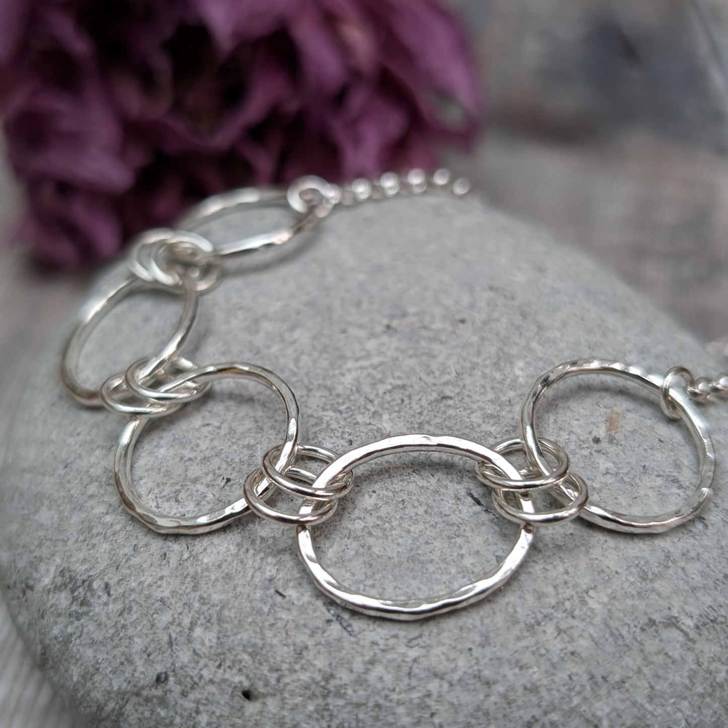 Five open silver circles with hammered finish linked with each other via two small silver circles in a repeating pattern. Each circle at each end of the pattern is attached to a silver chain. 