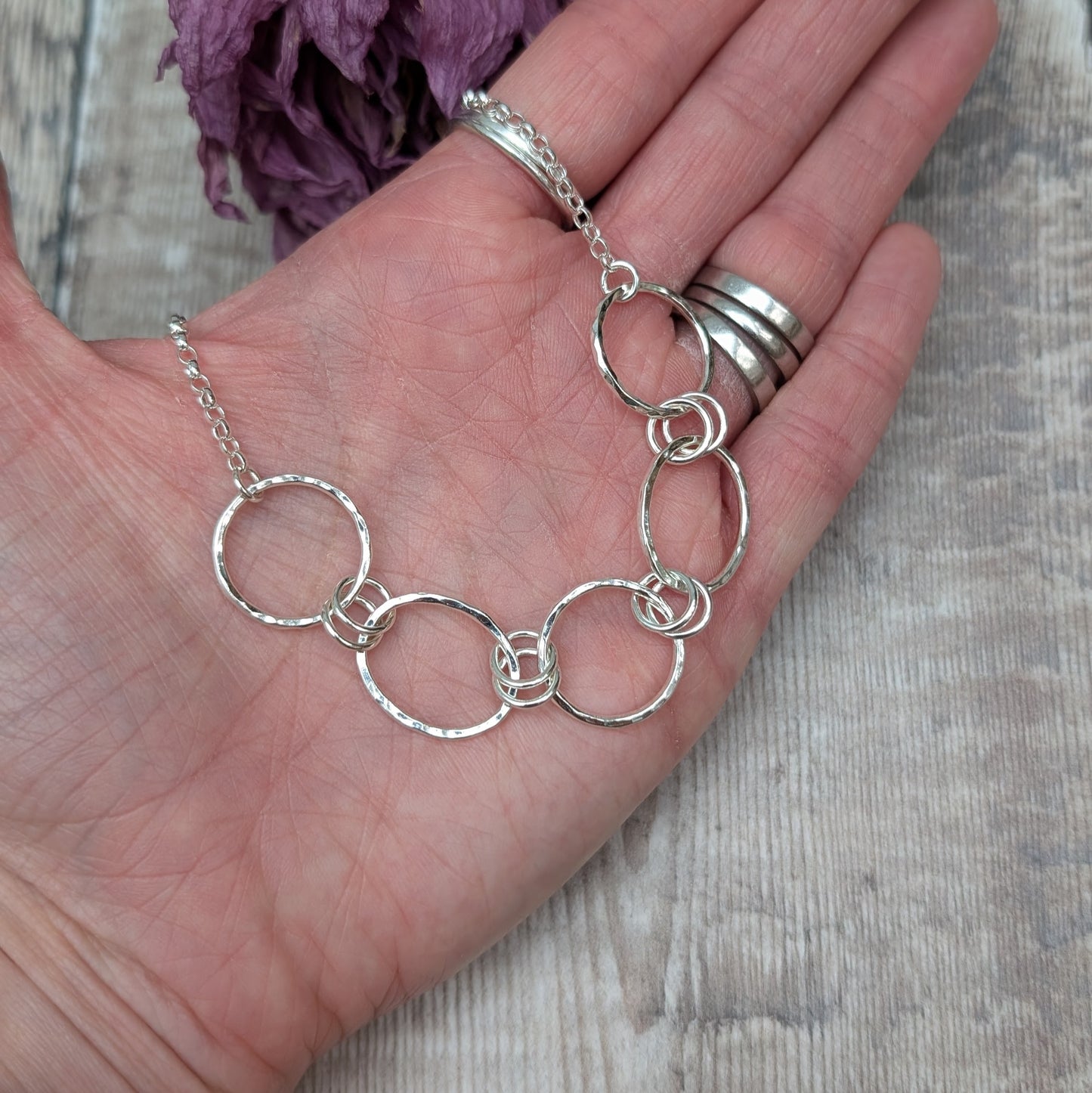 Five open silver circles with hammered finish linked with each other via two small silver circles in a repeating pattern. Each circle at each end of the pattern is attached to a silver chain. 