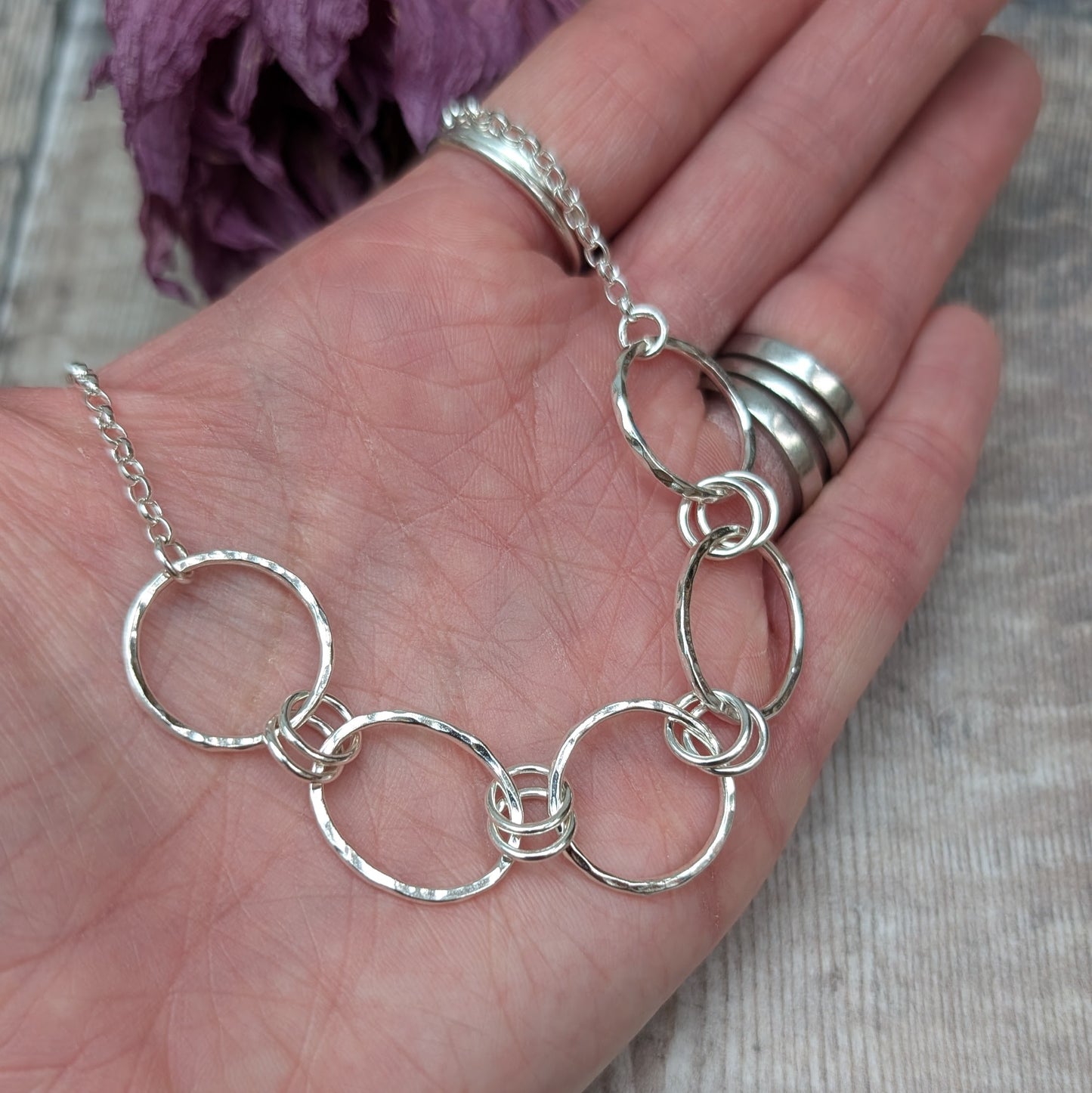 Five open silver circles with hammered finish linked with each other via two small silver circles in a repeating pattern. Each circle at each end of the pattern is attached to a silver chain. 