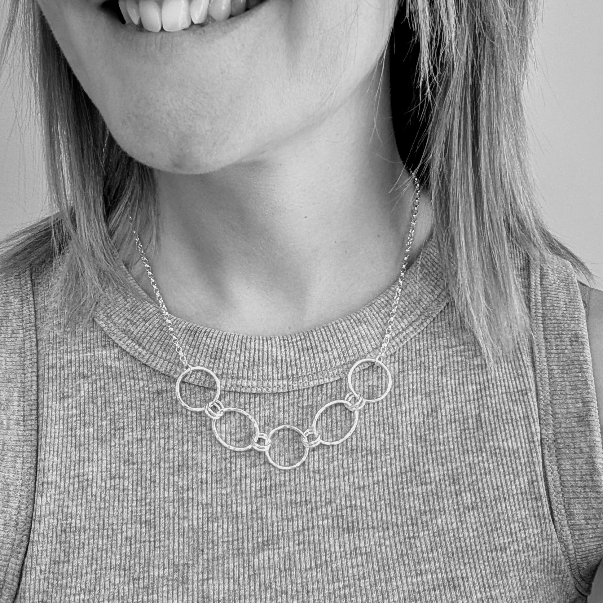 Five open silver circles with hammered finish linked with each other via two small silver circles in a repeating pattern. Each circle at each end of the pattern is attached to a silver chain. 