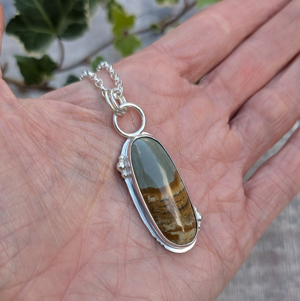 Owyhee Picture Jasper Statement Gemstone Necklace resting in the palm of a hand, showing the size of the long oval gemstone and handmade Sterling Silver setting.