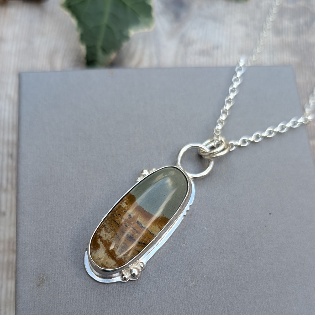 Owyhee Picture Jasper Statement Gemstone Necklace with a long oval gemstone featuring natural landscape patterns in green, brown and cream, surrounded by a handmade silver setting.