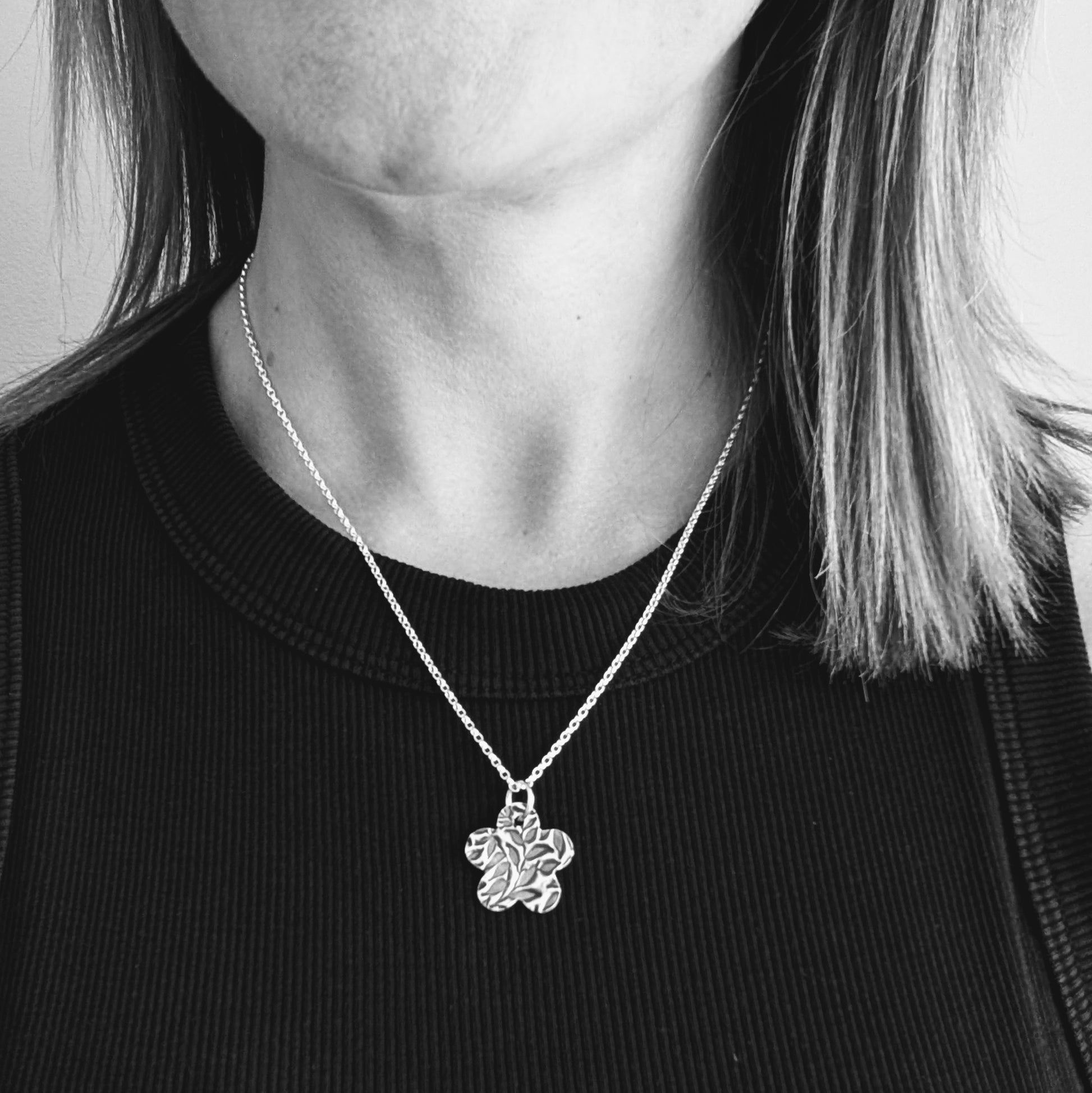 An oxidized silver pendant with a floral leaf pattern design shown being worn for size reference.