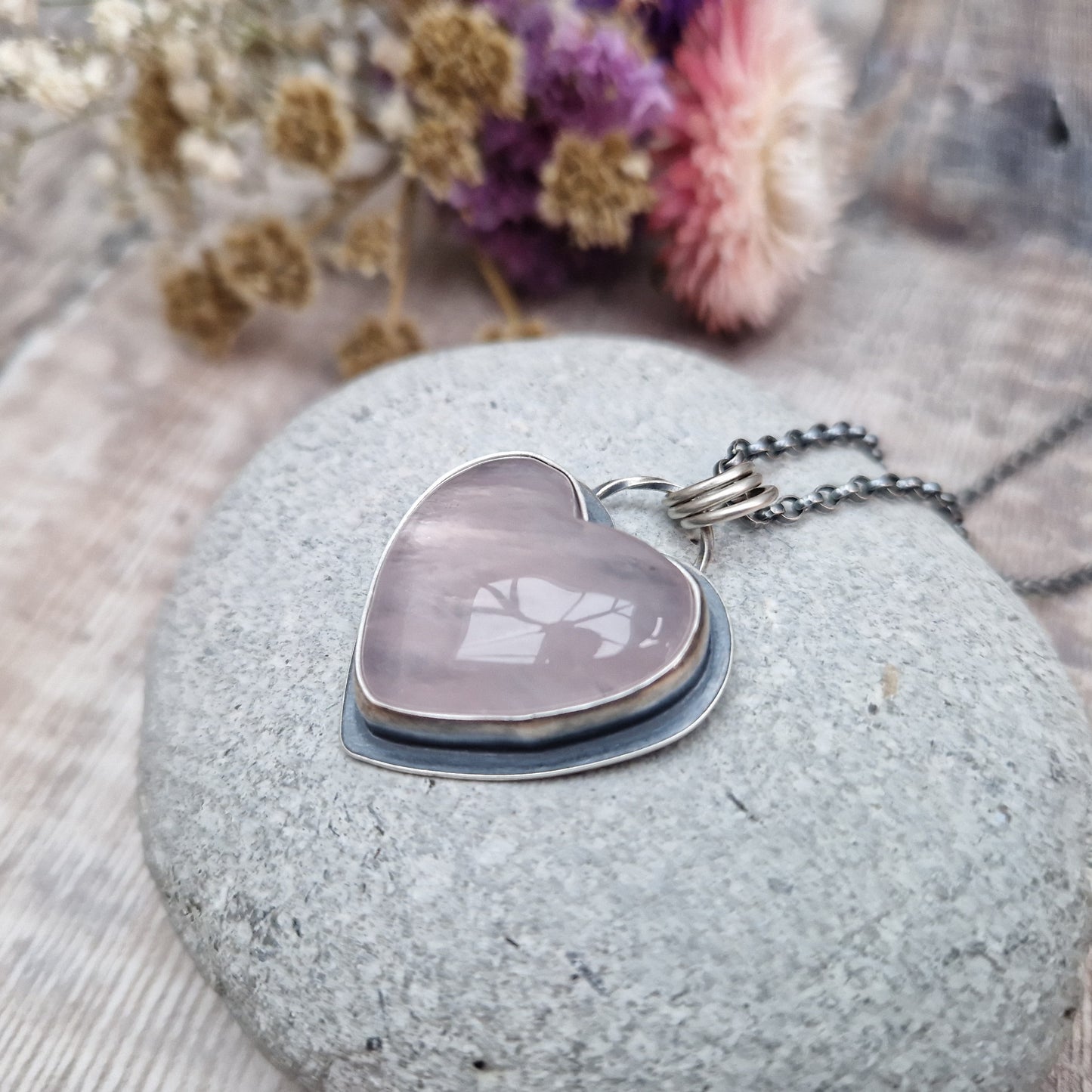 Rose Quartz heart shaped pendant set in oxidised Sterling Silver bezel surround, attached to an oxidised silver chain via three small circle links. The Rose Quartz has a smoky quality with diagonal flecks.