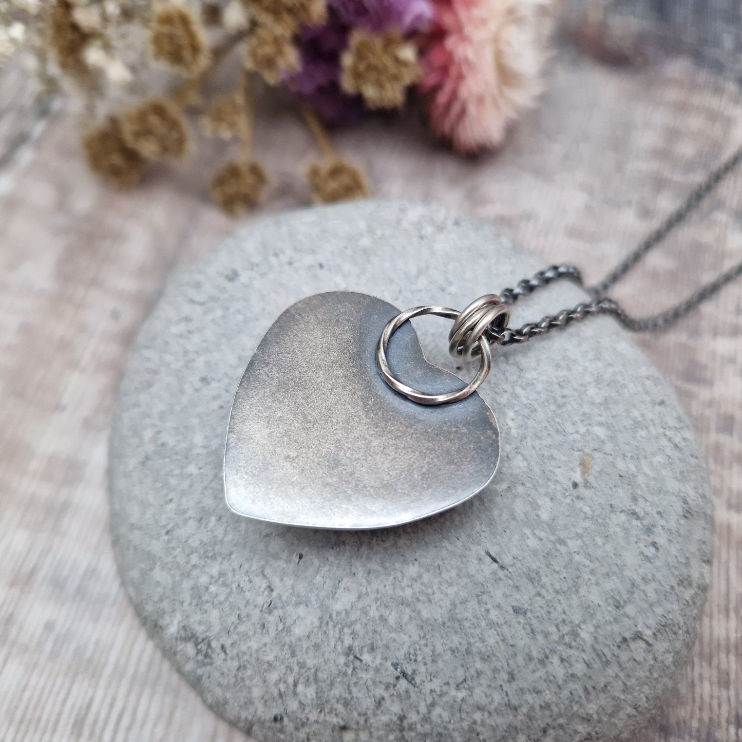 Rose Quartz heart shaped pendant set in oxidised Sterling Silver bezel surround, attached to an oxidised silver chain via three small circle links. The Rose Quartz has a smoky quality with diagonal flecks.