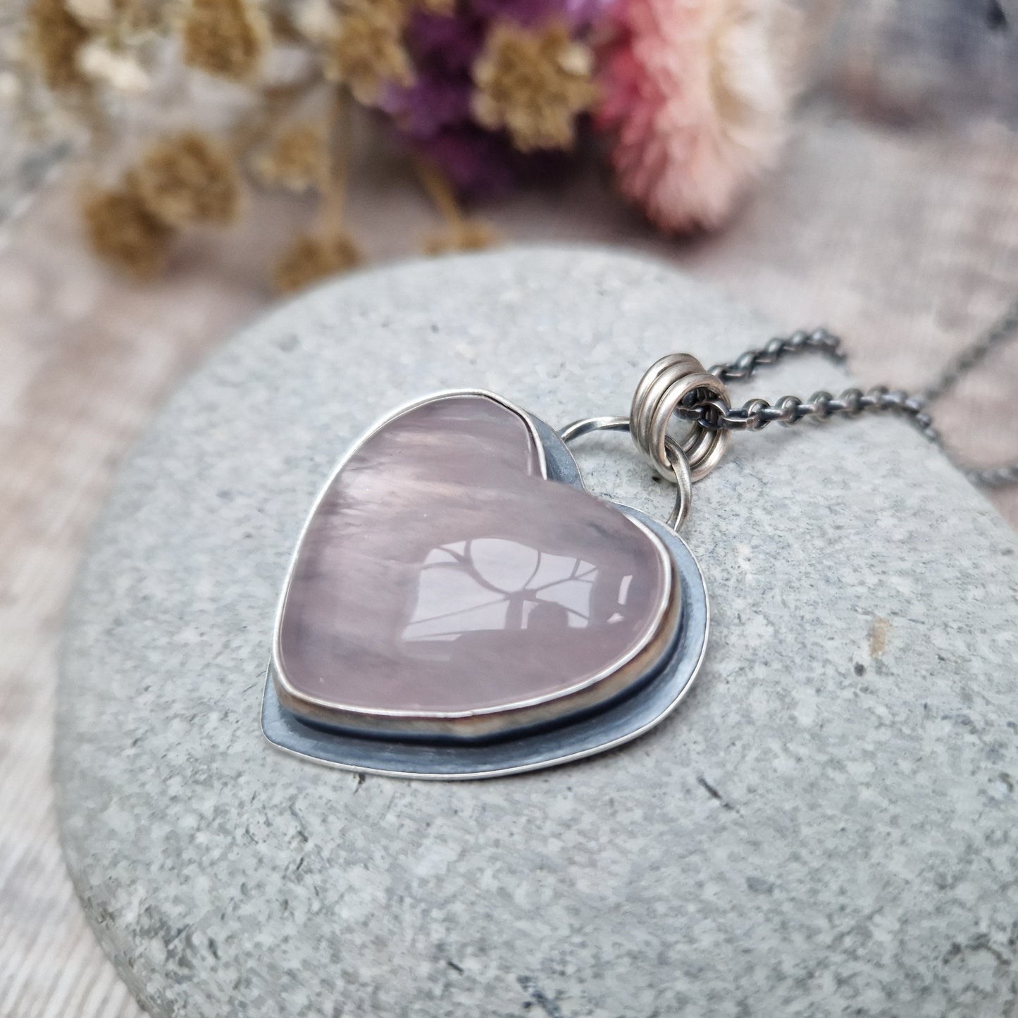 Rose Quartz heart shaped pendant set in oxidised Sterling Silver bezel surround, attached to an oxidised silver chain via three small circle links. The Rose Quartz has a smoky quality with diagonal flecks.