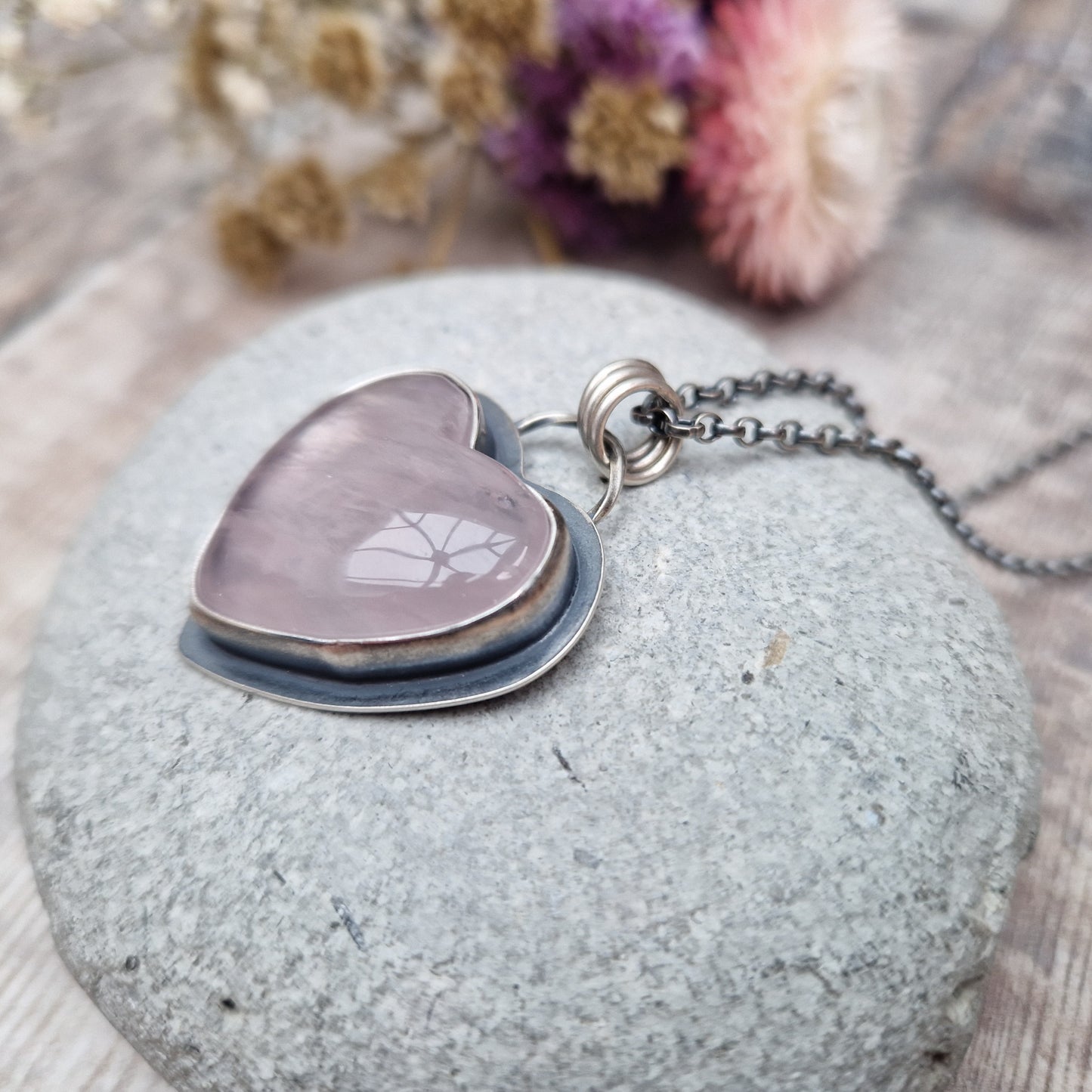 Rose Quartz heart shaped pendant set in oxidised Sterling Silver bezel surround, attached to an oxidised silver chain via three small circle links. The Rose Quartz has a smoky quality with diagonal flecks.