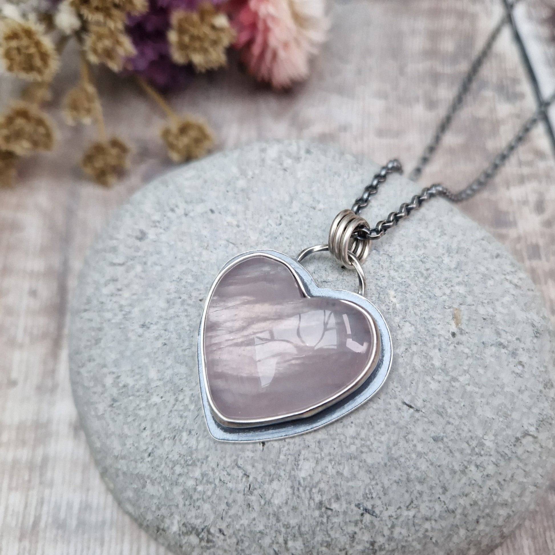 Rose Quartz heart shaped pendant set in oxidised Sterling Silver bezel surround, attached to an oxidised silver chain via three small circle links. The Rose Quartz has a smoky quality with diagonal flecks.