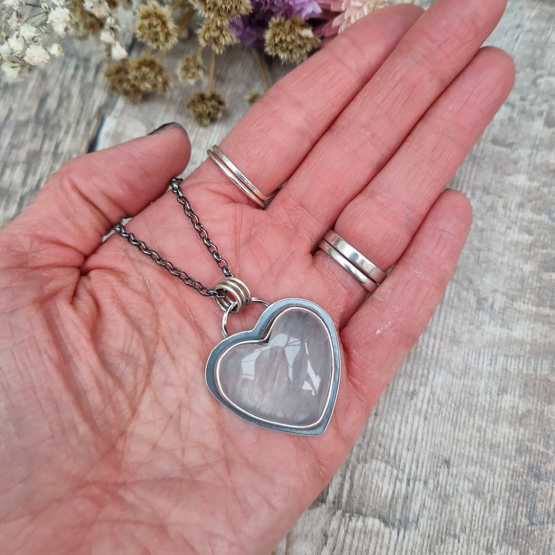 Rose Quartz heart shaped pendant set in oxidised Sterling Silver bezel surround, attached to an oxidised silver chain via three small circle links. The Rose Quartz has a smoky quality with diagonal flecks.