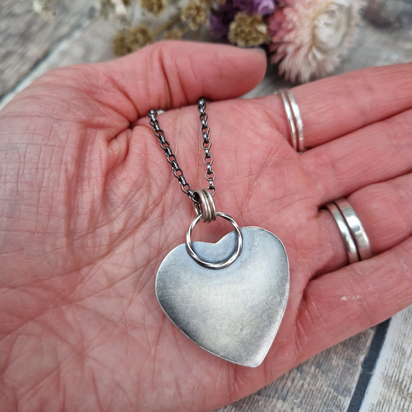 Rose Quartz heart shaped pendant set in oxidised Sterling Silver bezel surround, attached to an oxidised silver chain via three small circle links. The Rose Quartz has a smoky quality with diagonal flecks.