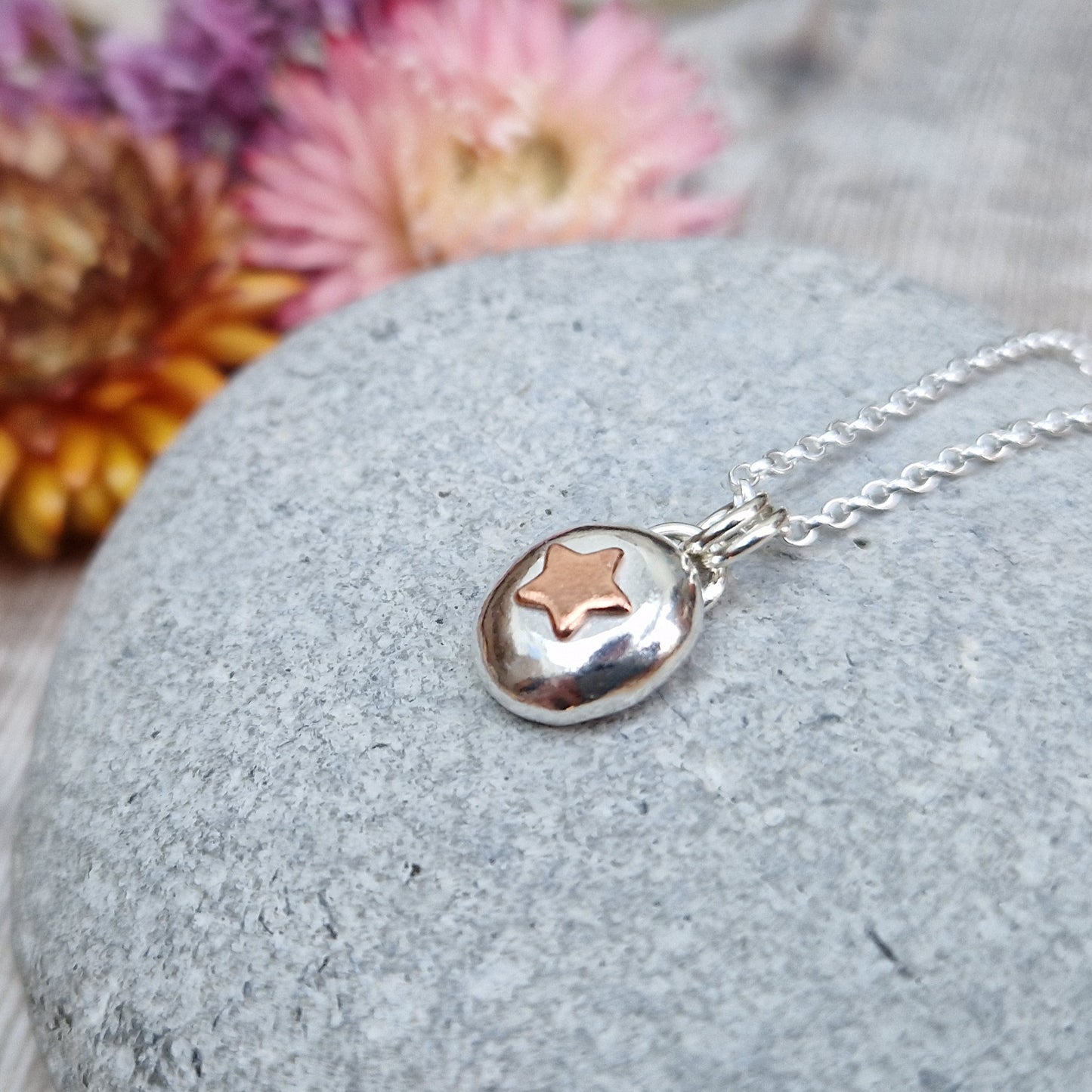 Sterling Silver round pebble shaped pendant with a slightly raised copper star shape at its centre. Suspended from silver chain via two small circle links.