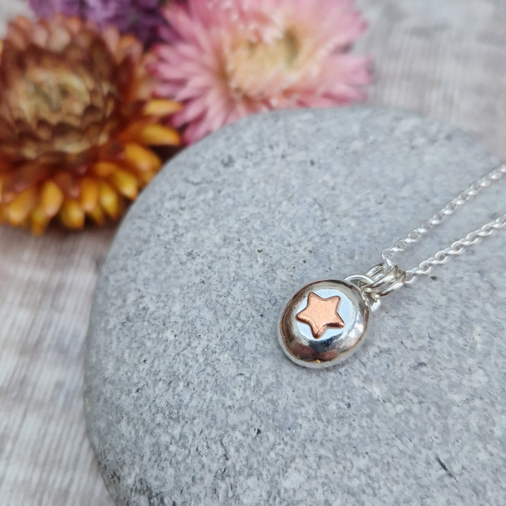 Sterling Silver round pebble shaped pendant with a slightly raised copper star shape at its centre. Suspended from silver chain via two small circle links.