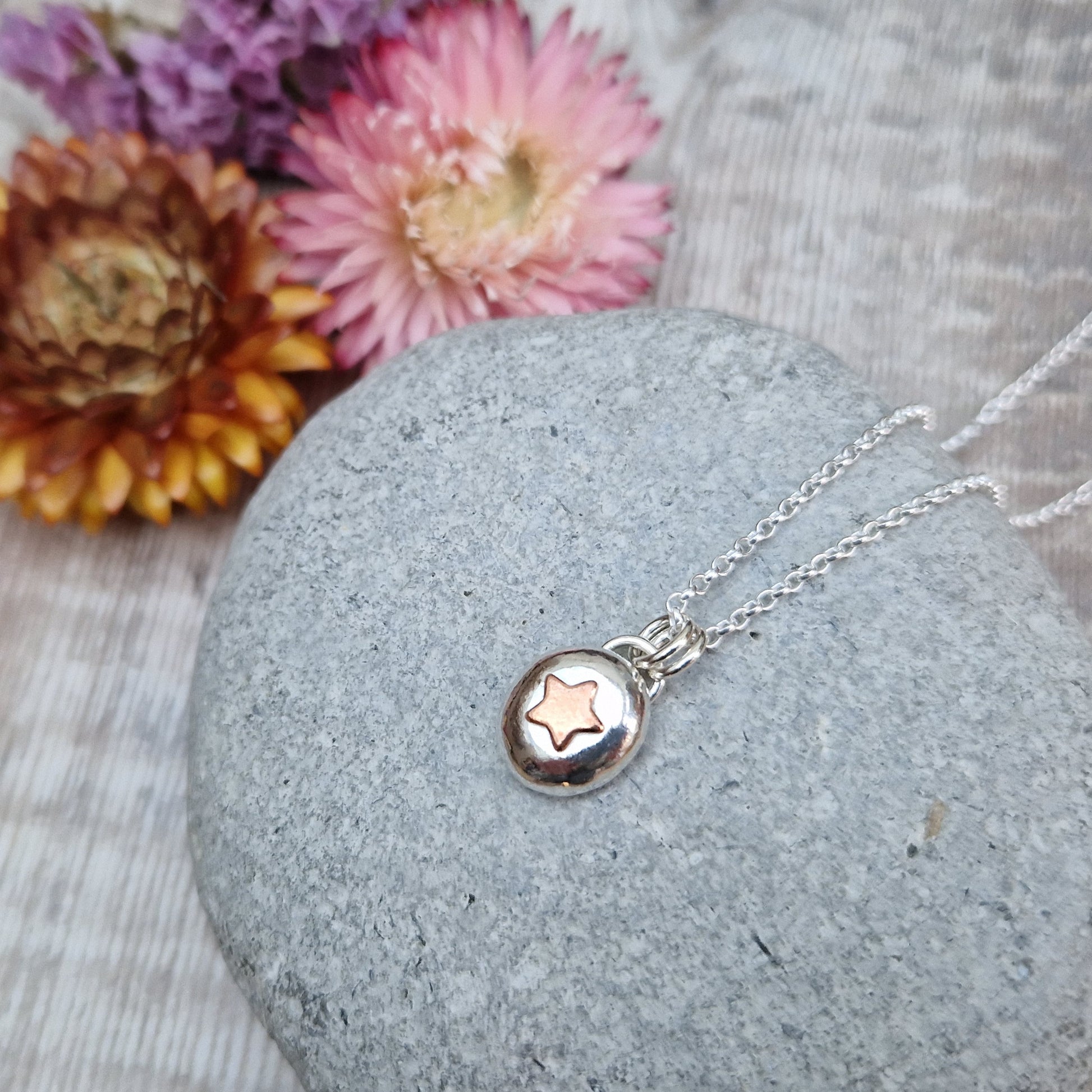 Sterling Silver round pebble shaped pendant with a slightly raised copper star shape at its centre. Suspended from silver chain via two small circle links.