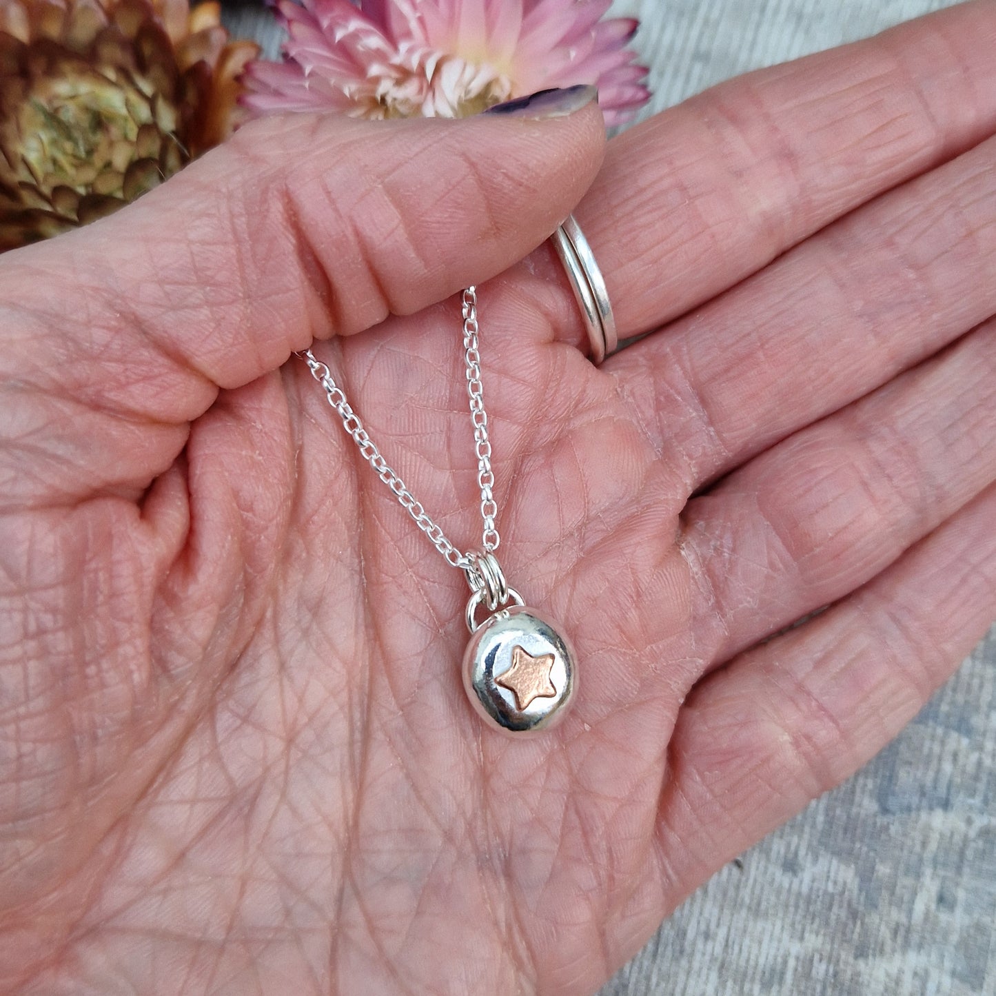 Sterling Silver round pebble shaped pendant with a slightly raised copper star shape at its centre. Suspended from silver chain via two small circle links.