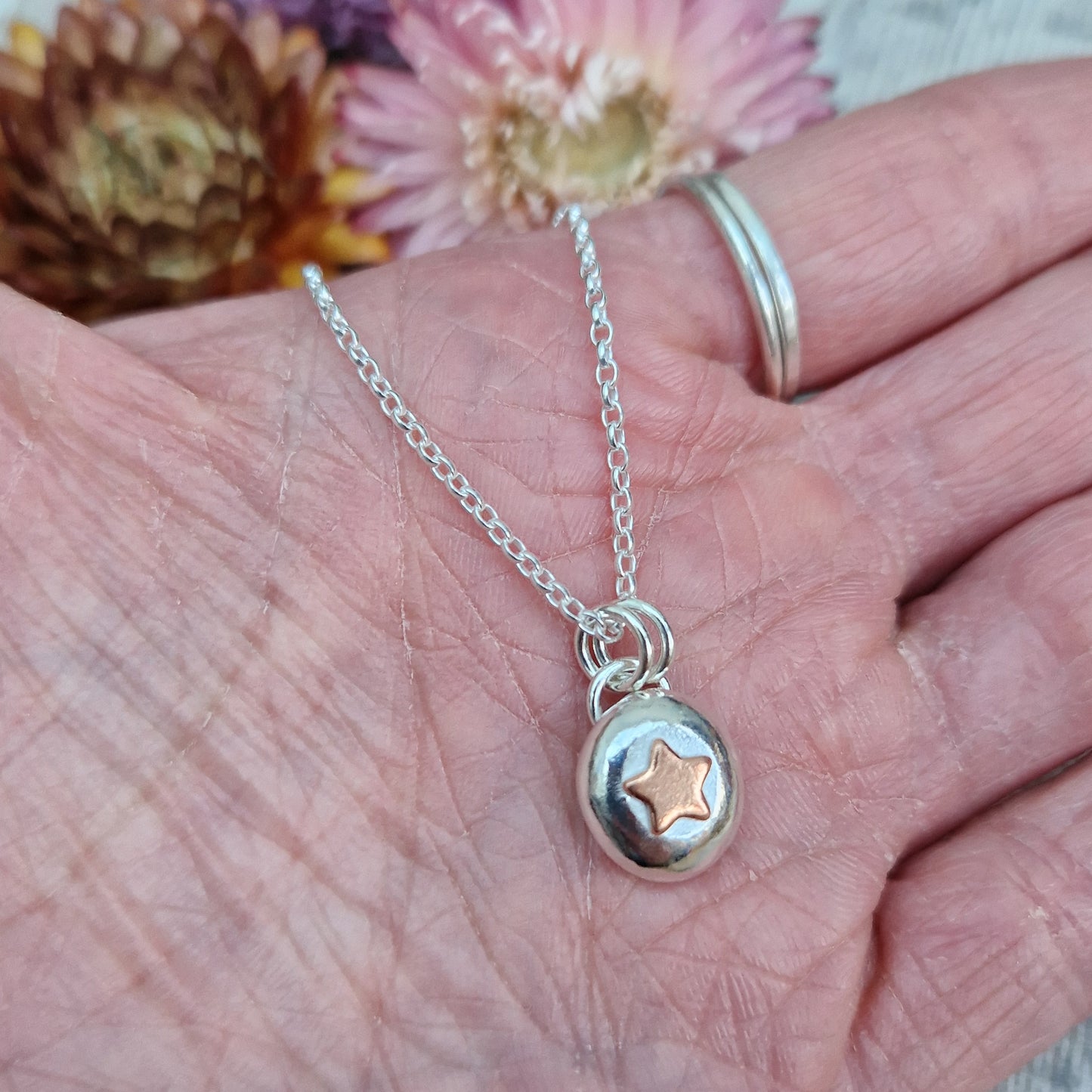 Sterling Silver round pebble shaped pendant with a slightly raised copper star shape at its centre. Suspended from silver chain via two small circle links.