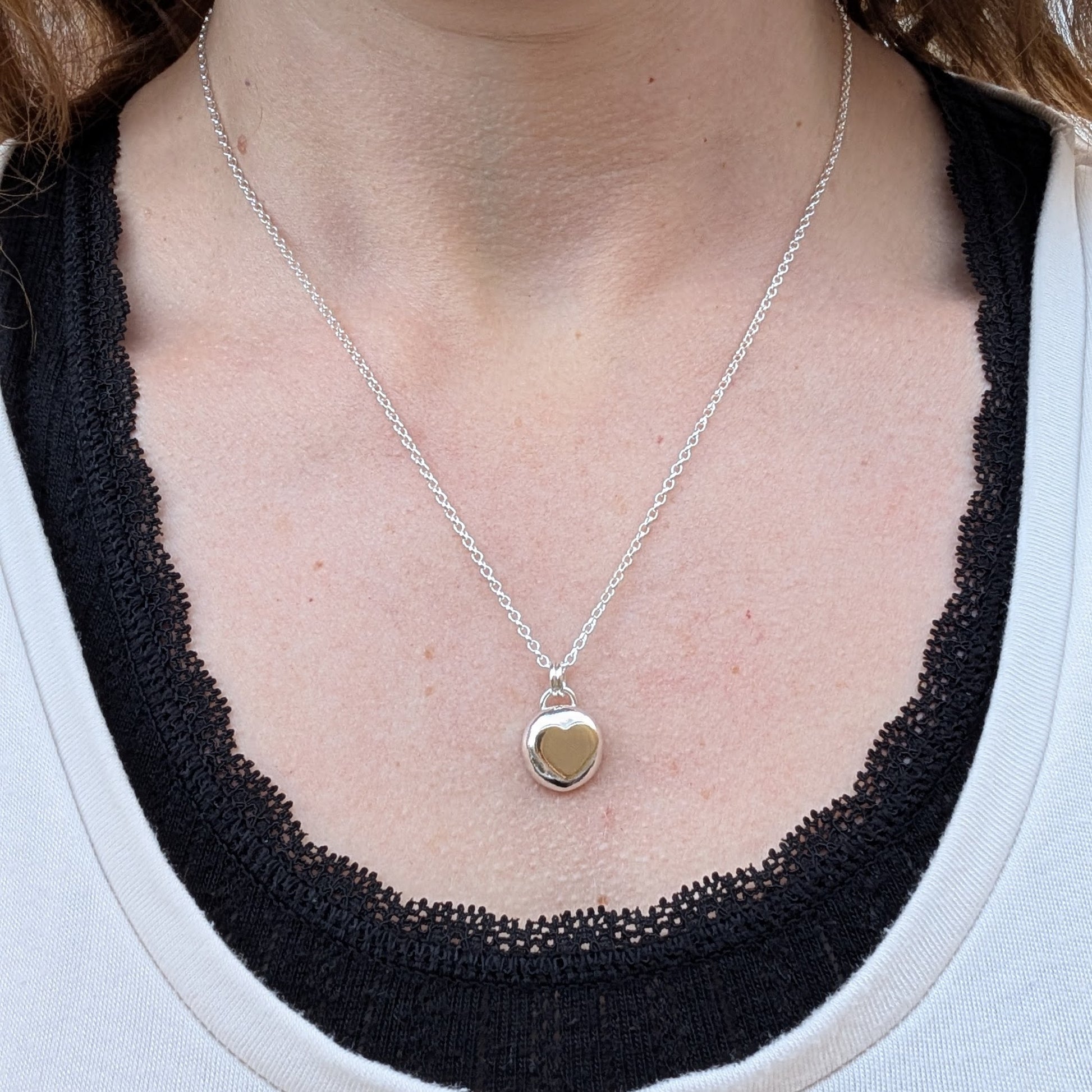 Recycled sterling silver pebble necklace with a 9ct recycled gold heart, displayed on a person’s neckline. The pendant is worn on a dainty silver chain, highlighting its elegant and minimalist design.