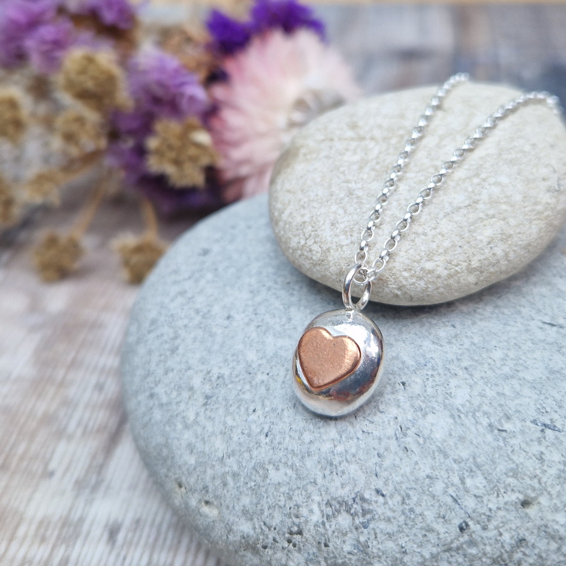 Sterling Silver round pebble shaped pendant with slightly raised silver heart shape at its centre. Suspended from silver chain via small circle link.